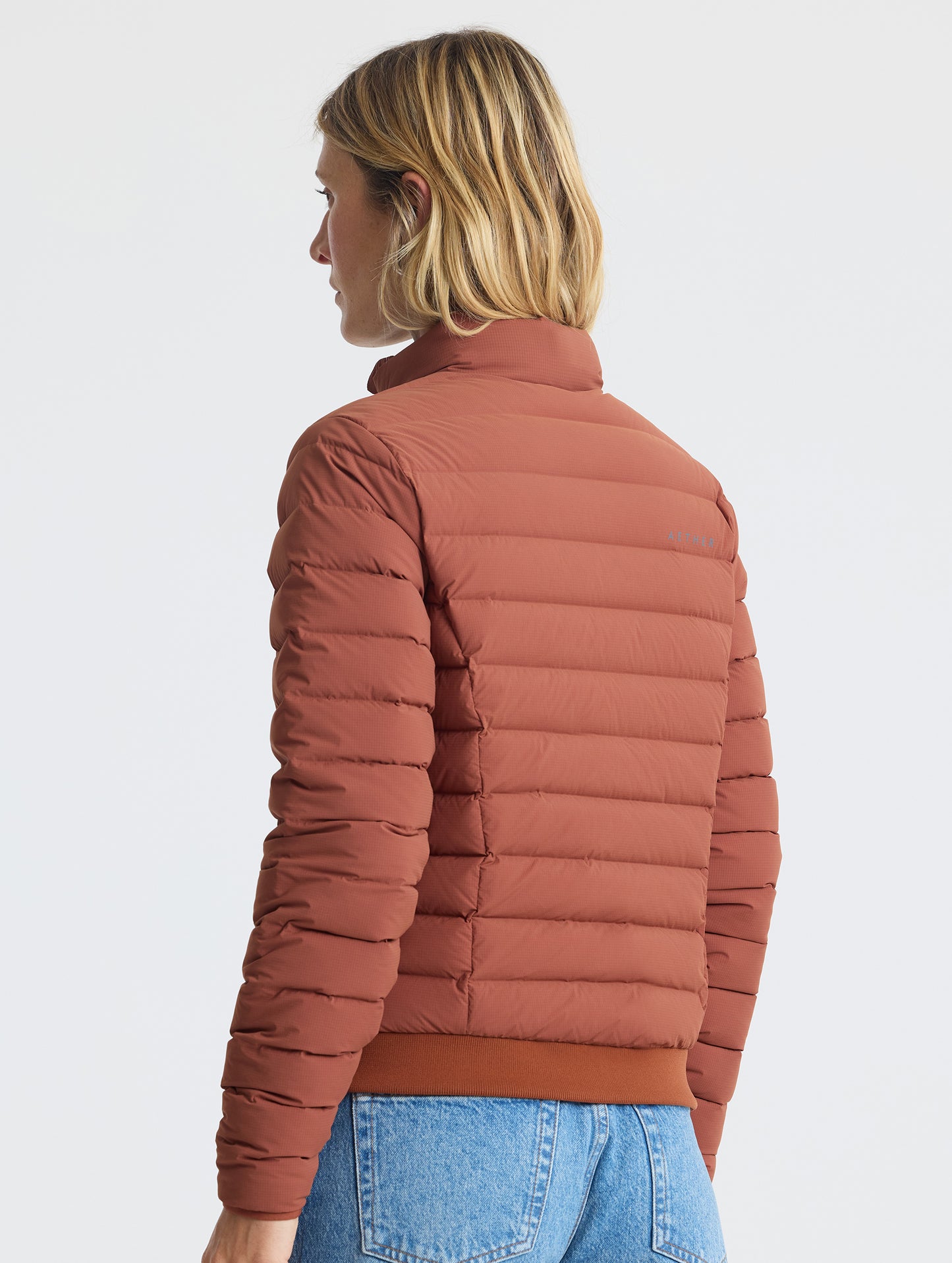 Rear angled view of woman wearing W Launch Full-Zip Jacket NH in Redwood Rust from AETHER Apparel.