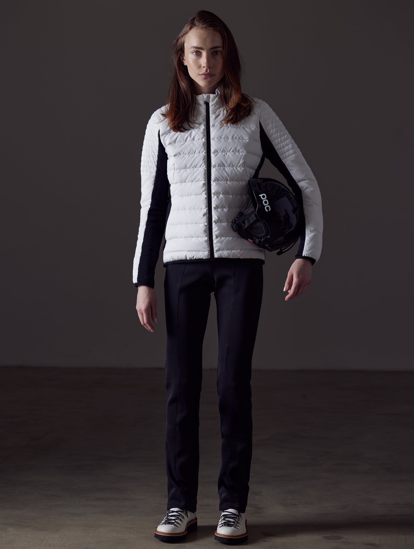 Front full-body view of woman holding helmet under arm wearing Ozone Jacket in White from AETHER Apparel.