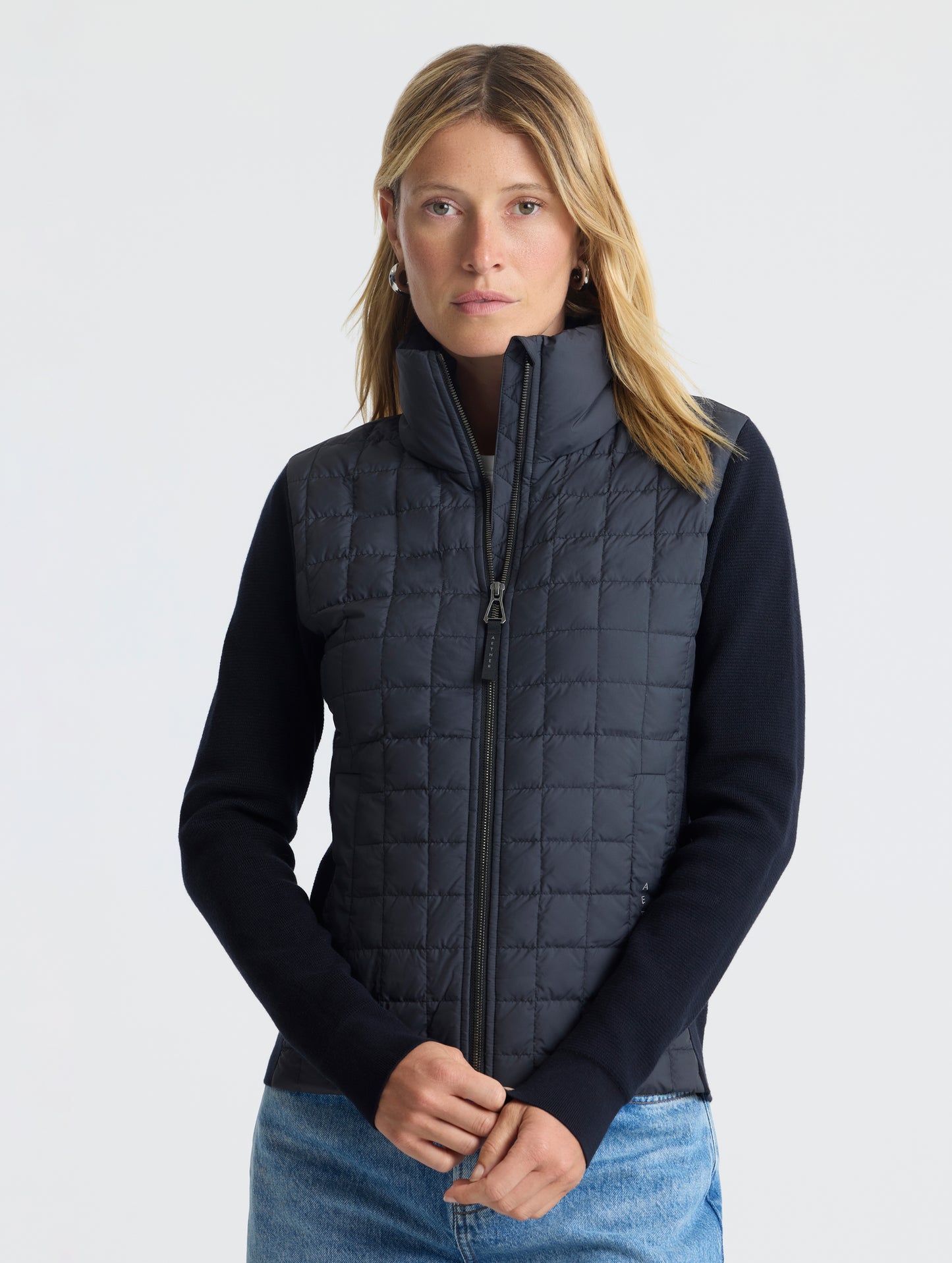Front, upper-body view of woman wearing zipped-up Phase Full-Zip in Onyx Black from AETHER Apparel.