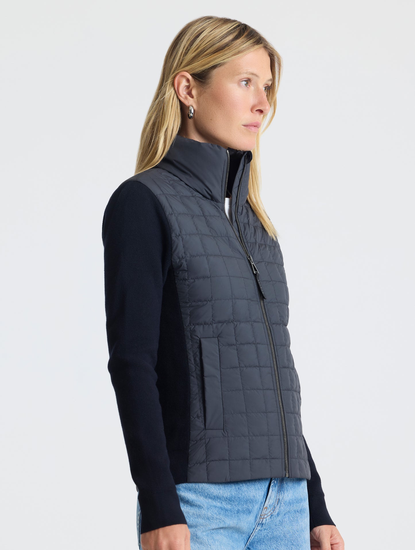 Front, angled, upper-body view of woman wearing zipped-up Phase Full-Zip in Onyx Black from AETHER Apparel.