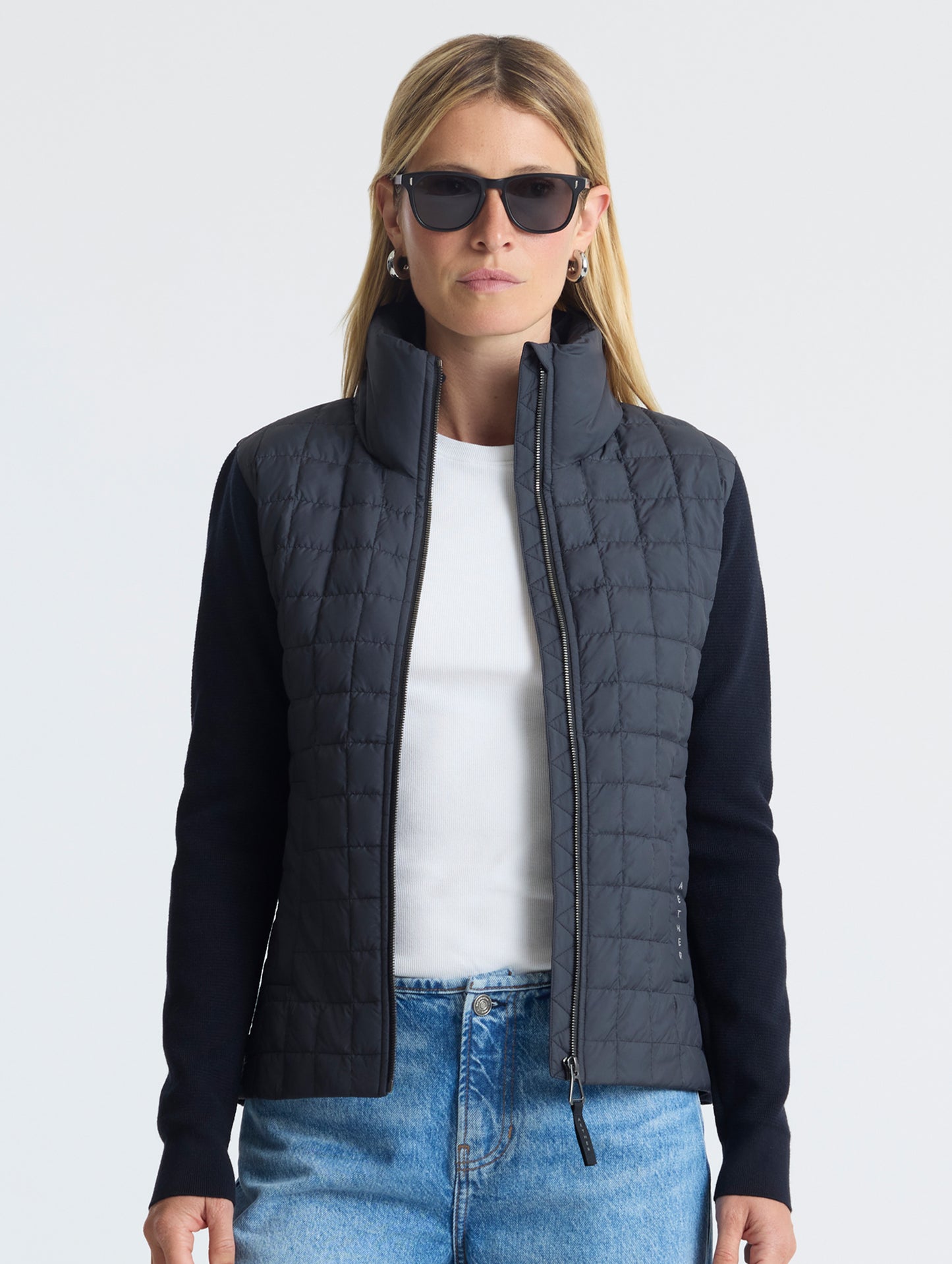 Front, upper-body view of woman wearing unzipped Phase Full-Zip in Onyx Black from AETHER Apparel.
