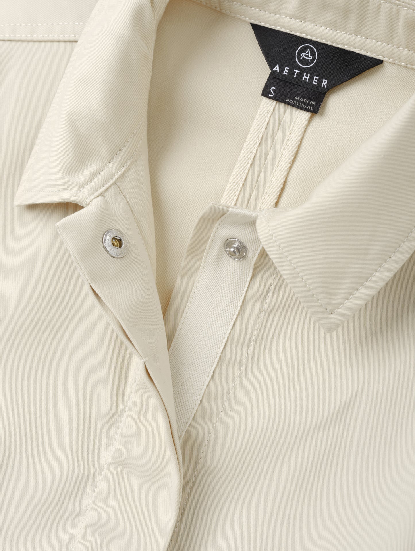 Closeup detailed view of the main center-front snap closure on the Raven Waxed Cotton Jacket in Bone from AETHER Apparel.