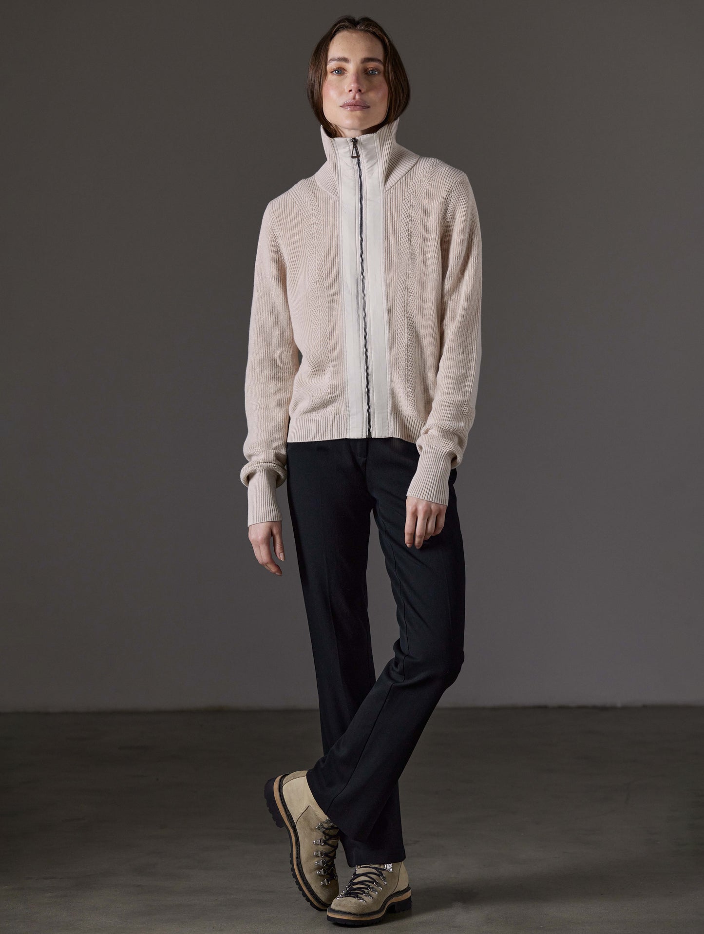 Front full-body view of woman standing with legs crossed wearing Rhea Full-Zip Sweater in Bone white from AETHER Apparel.