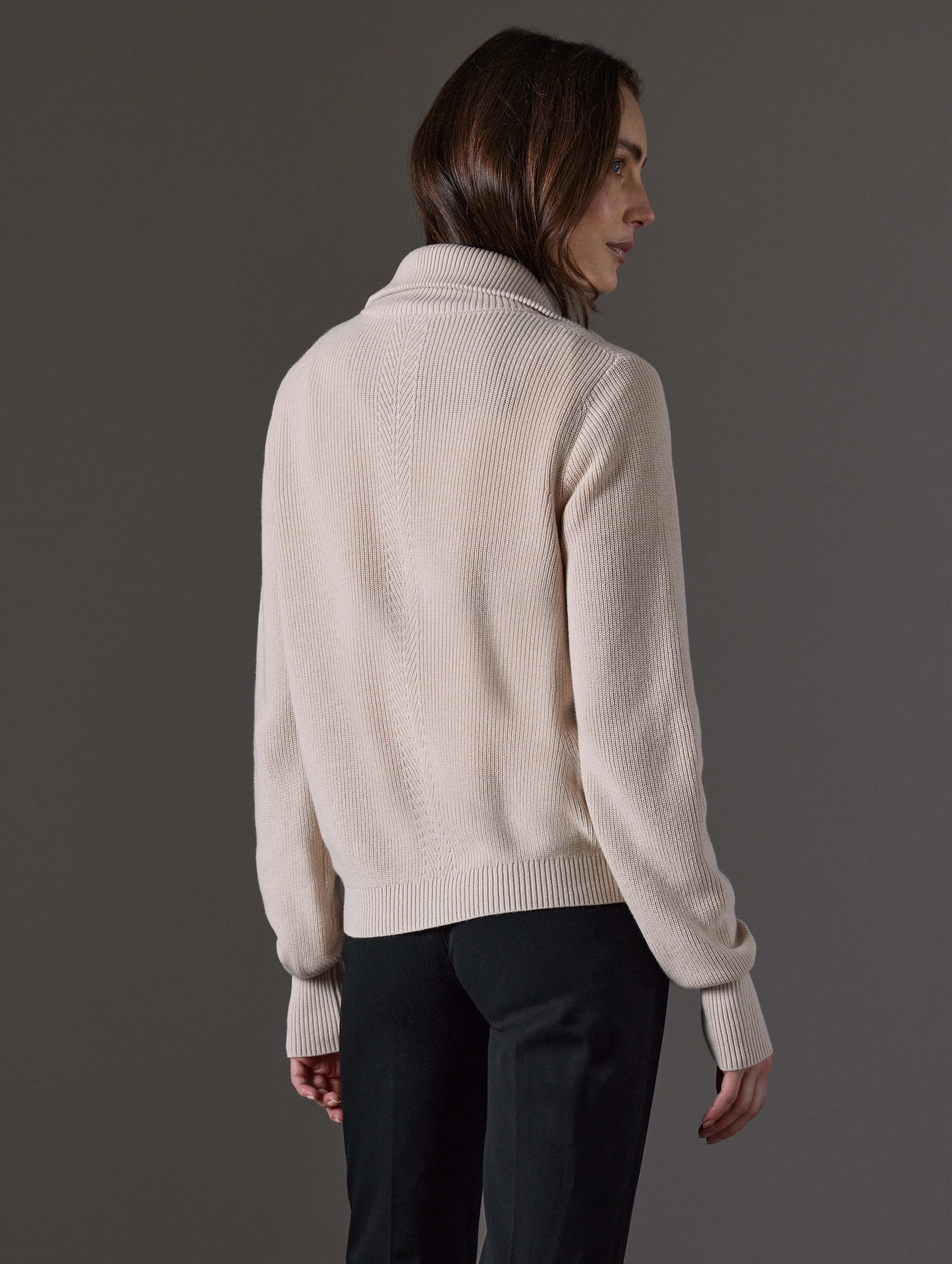 Rear angled view of woman wearing Rhea Full-Zip Sweater in Bone white from AETHER Apparel.