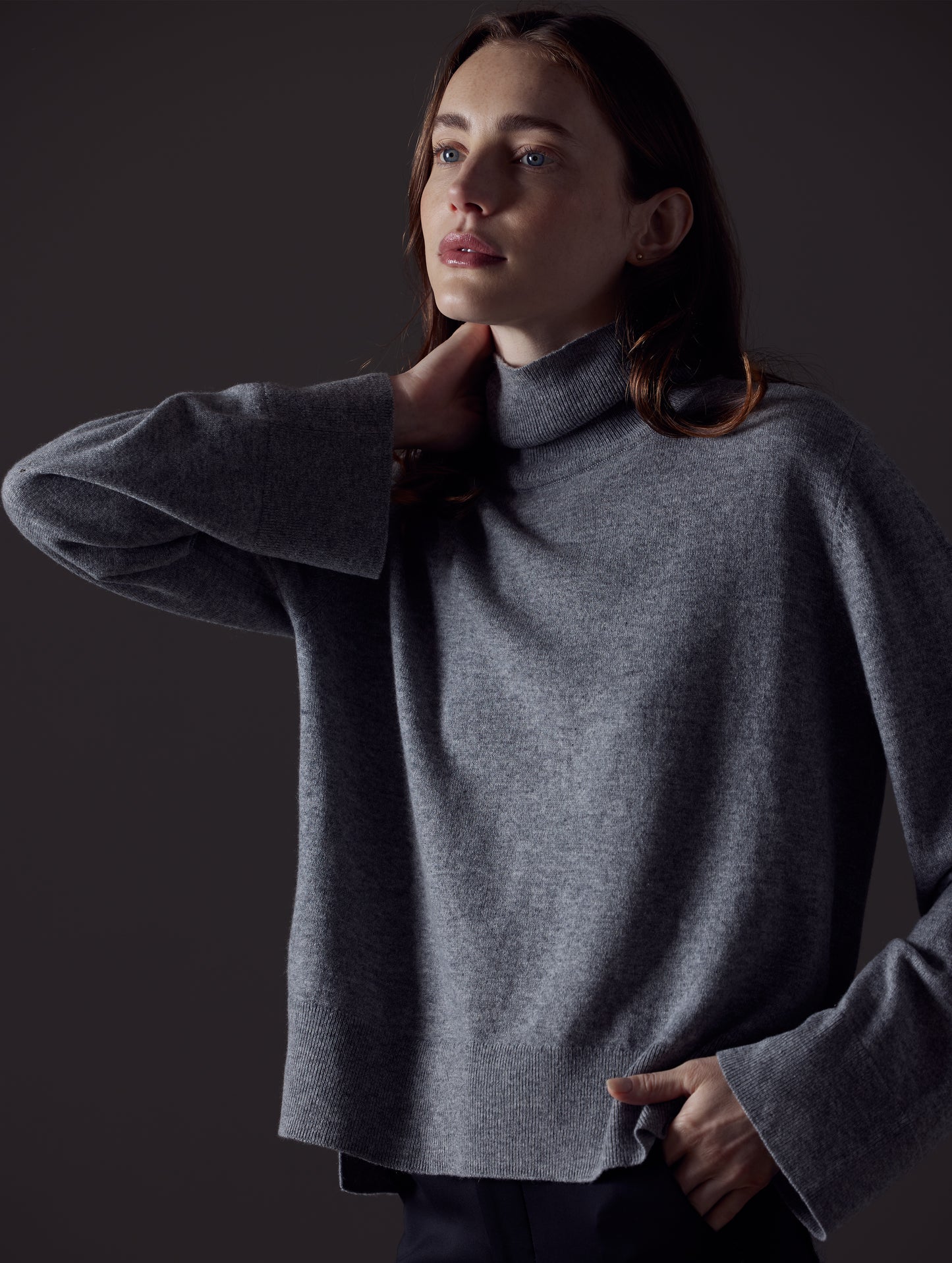 Front angled view of woman with hand on collar wearing Leigh Cashmere Turtleneck Sweater in Heather Grey from AETHER Apparel.