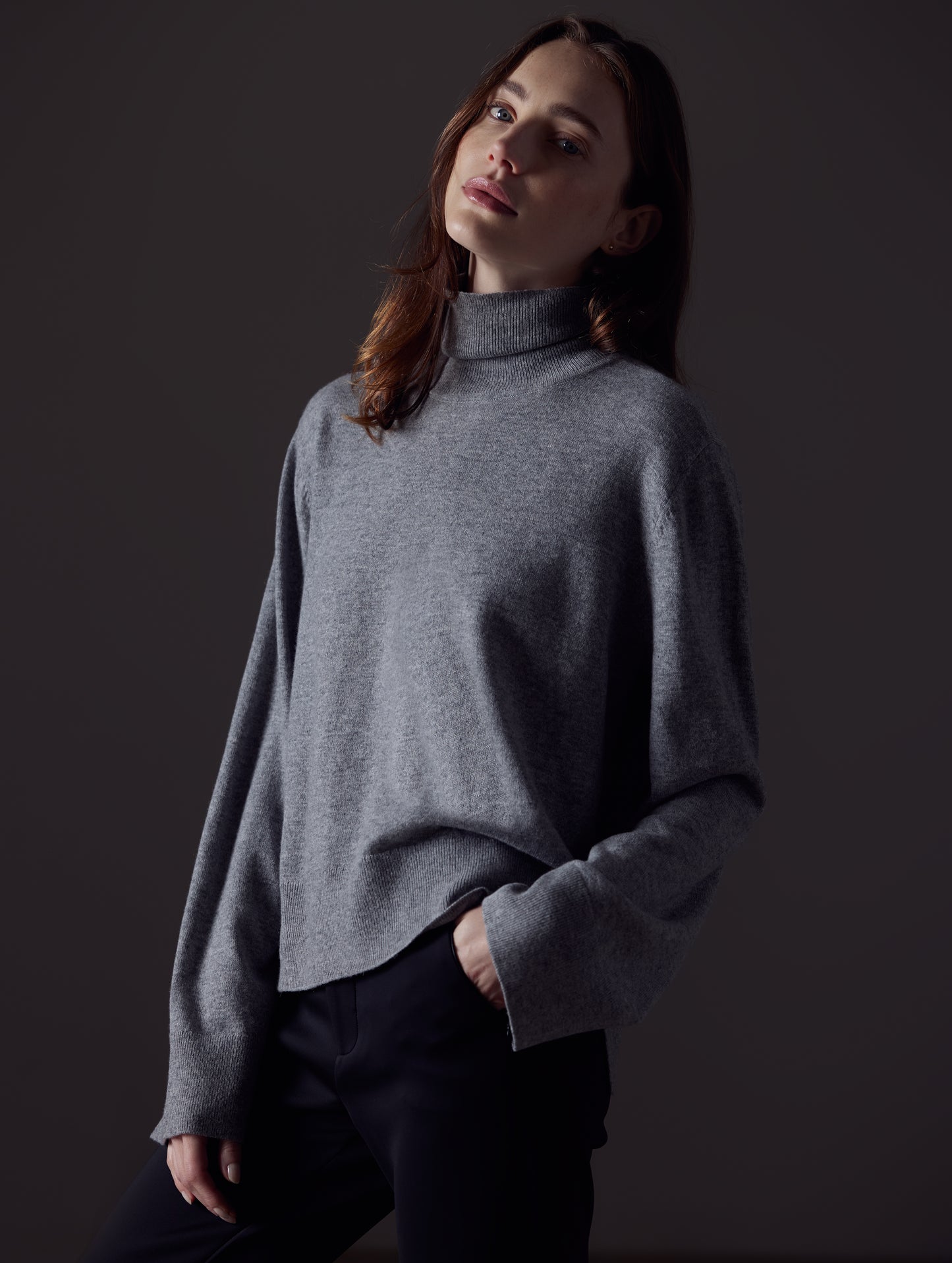 Front angled view of woman with hand in pant pocket wearing Leigh Cashmere Turtleneck Sweater in Heather Grey from AETHER Apparel.
