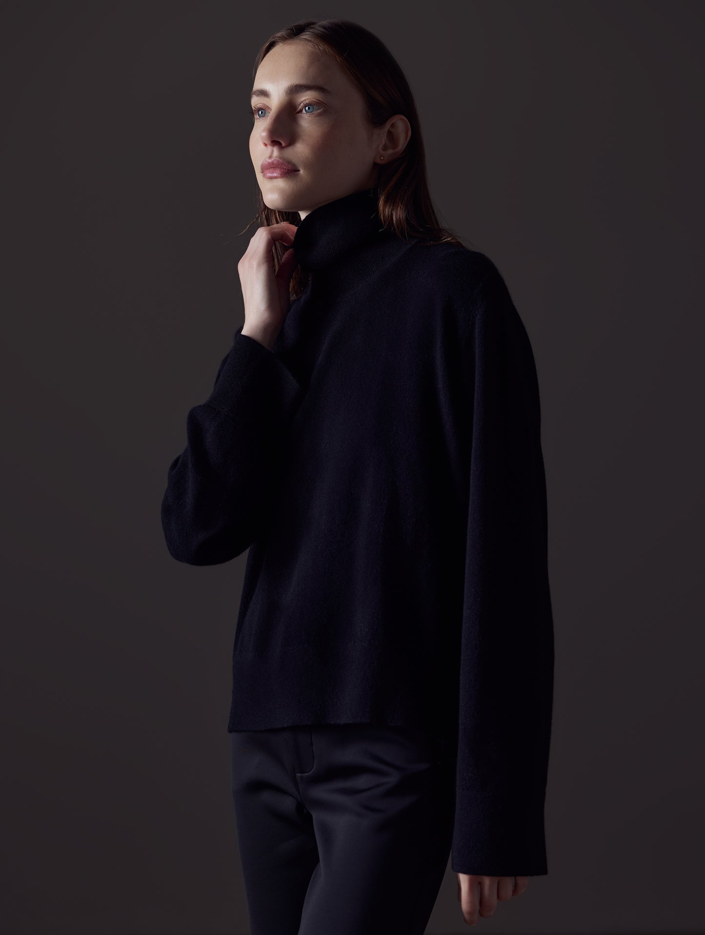 Front angled view of woman with hand on collar wearing Leigh Cashmere Turtleneck Sweater in Onyx Black from AETHER Apparel.