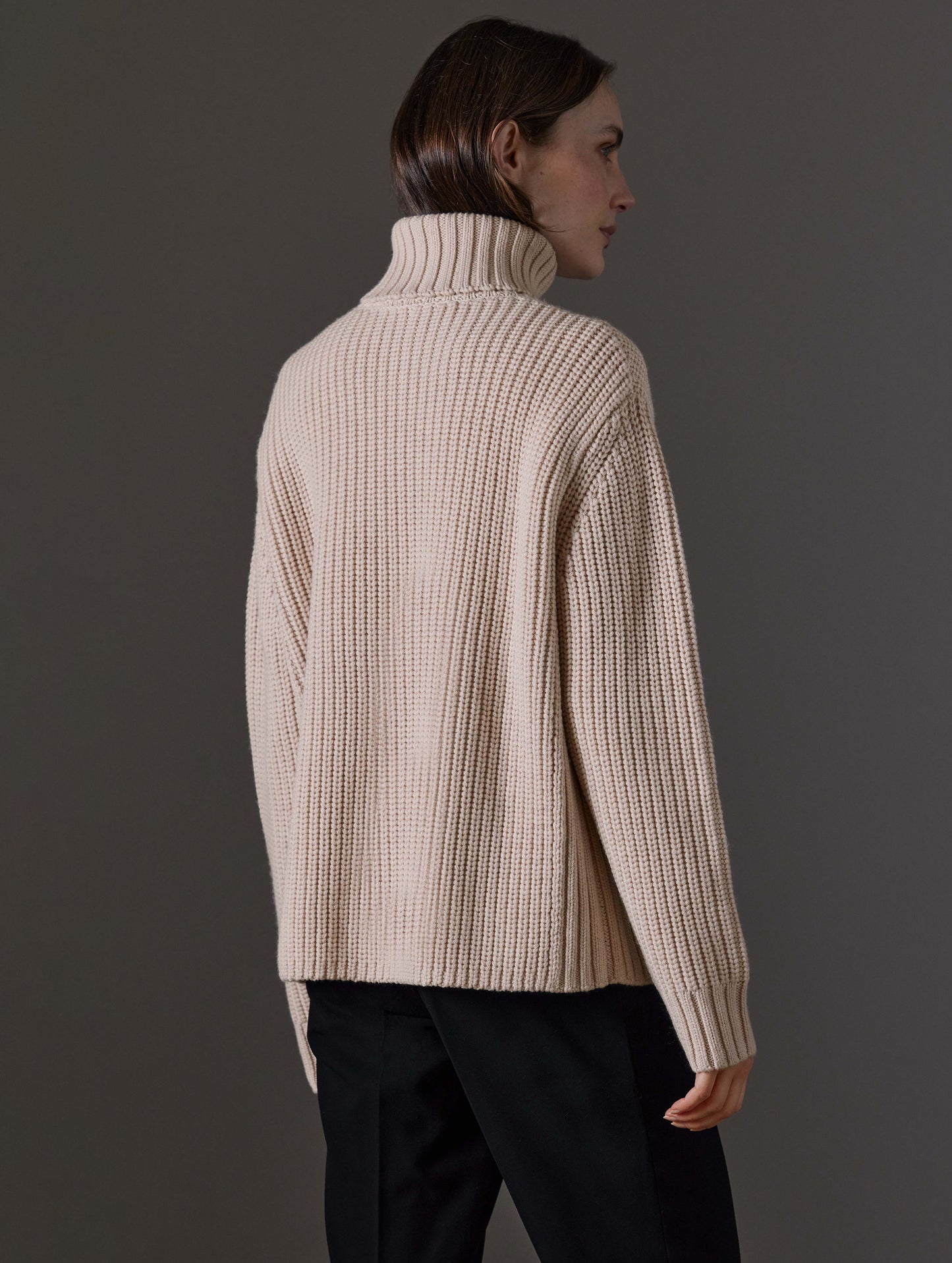 Rear angled view of woman wearing Sherwood Turtleneck Sweater in Blush beige from AETHER Apparel.