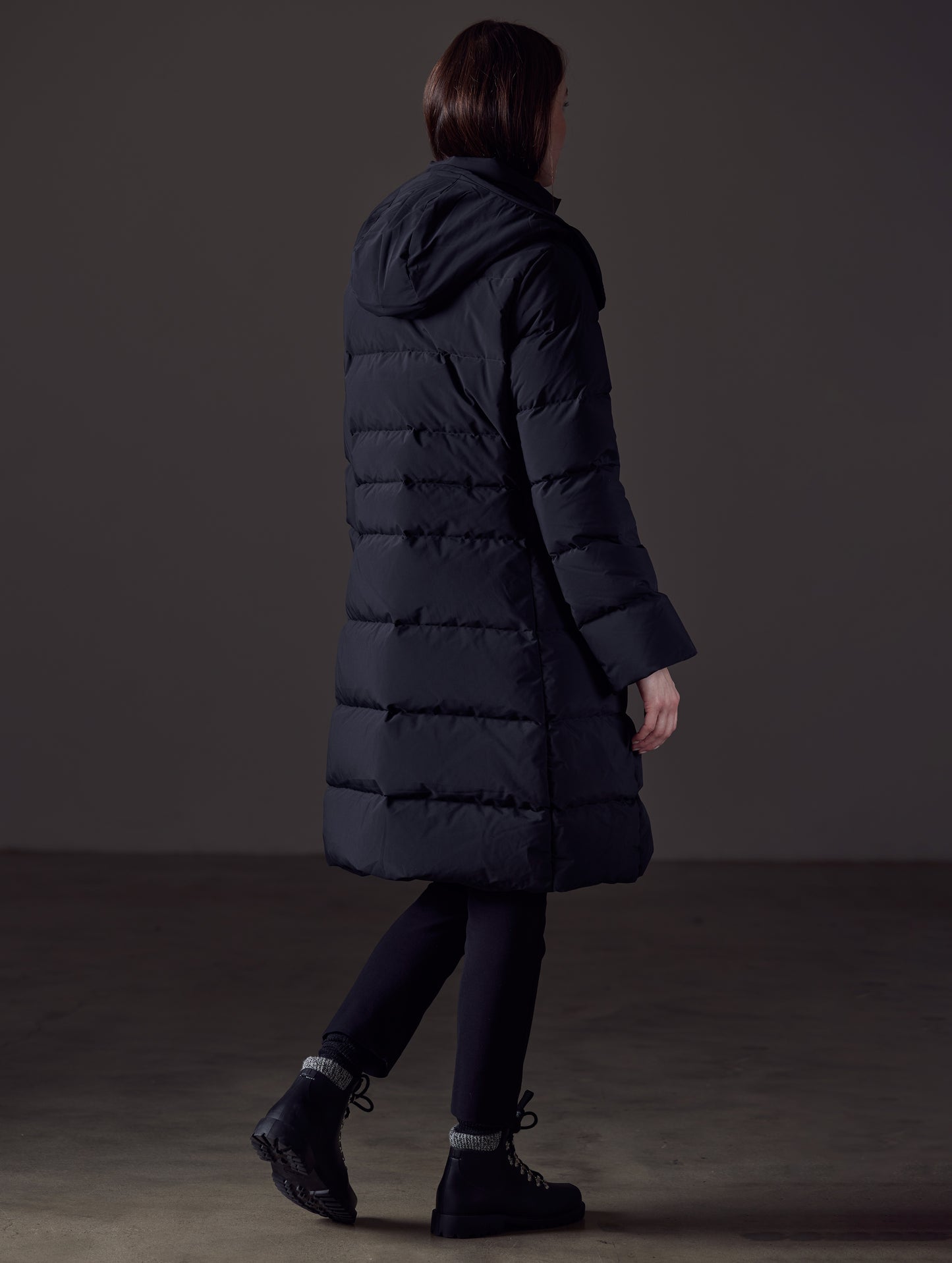 Rear angled full-body view of woman wearing Stirling Jacket in Onyx Black from AETHER Apparel.