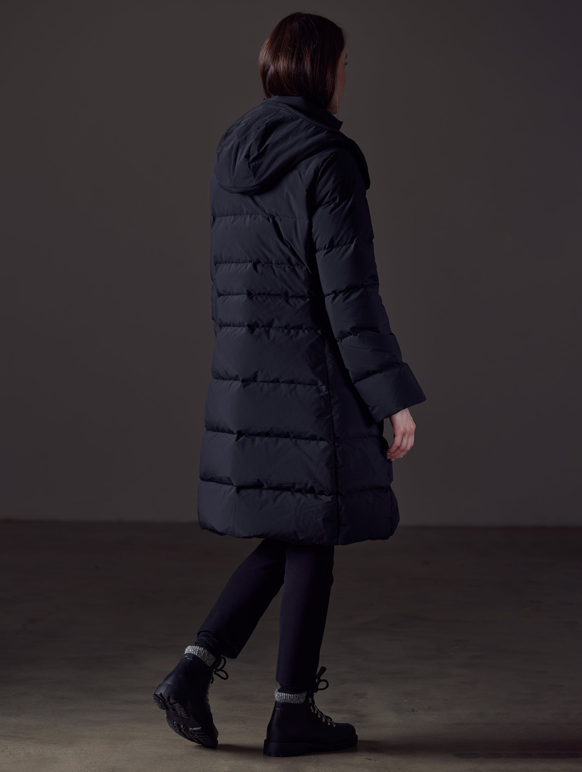 Rear angled full-body view of woman wearing Stirling Jacket in Onyx Black from AETHER Apparel.