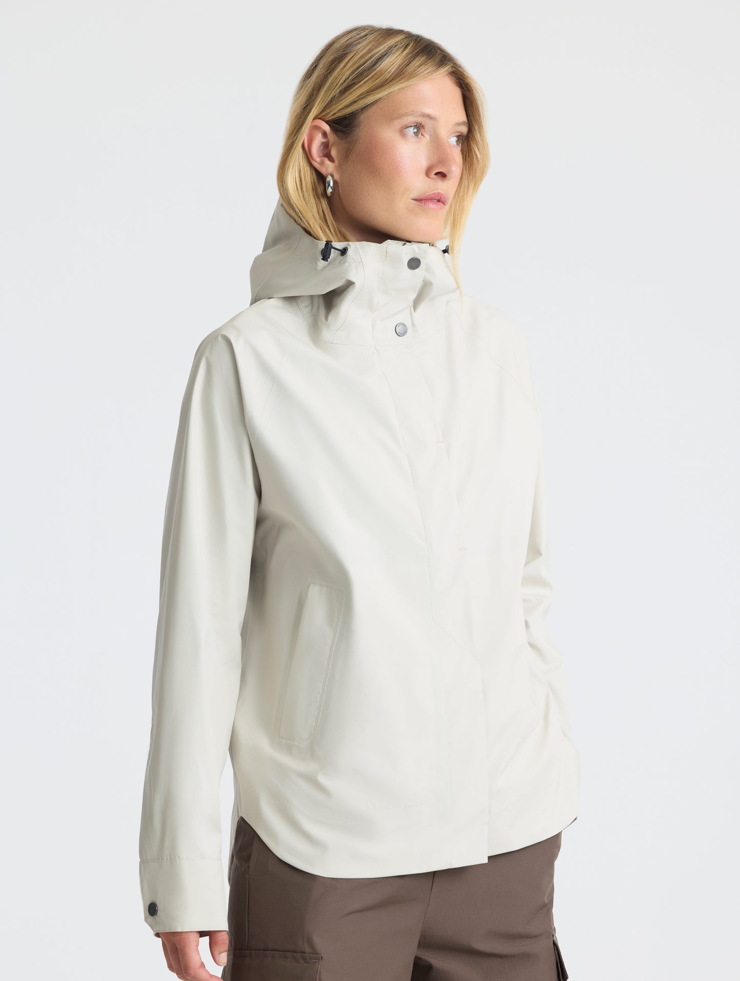 Right-angled view of woman wearing Storm All-Weather Jacket in Bone white from AETHER Apparel.