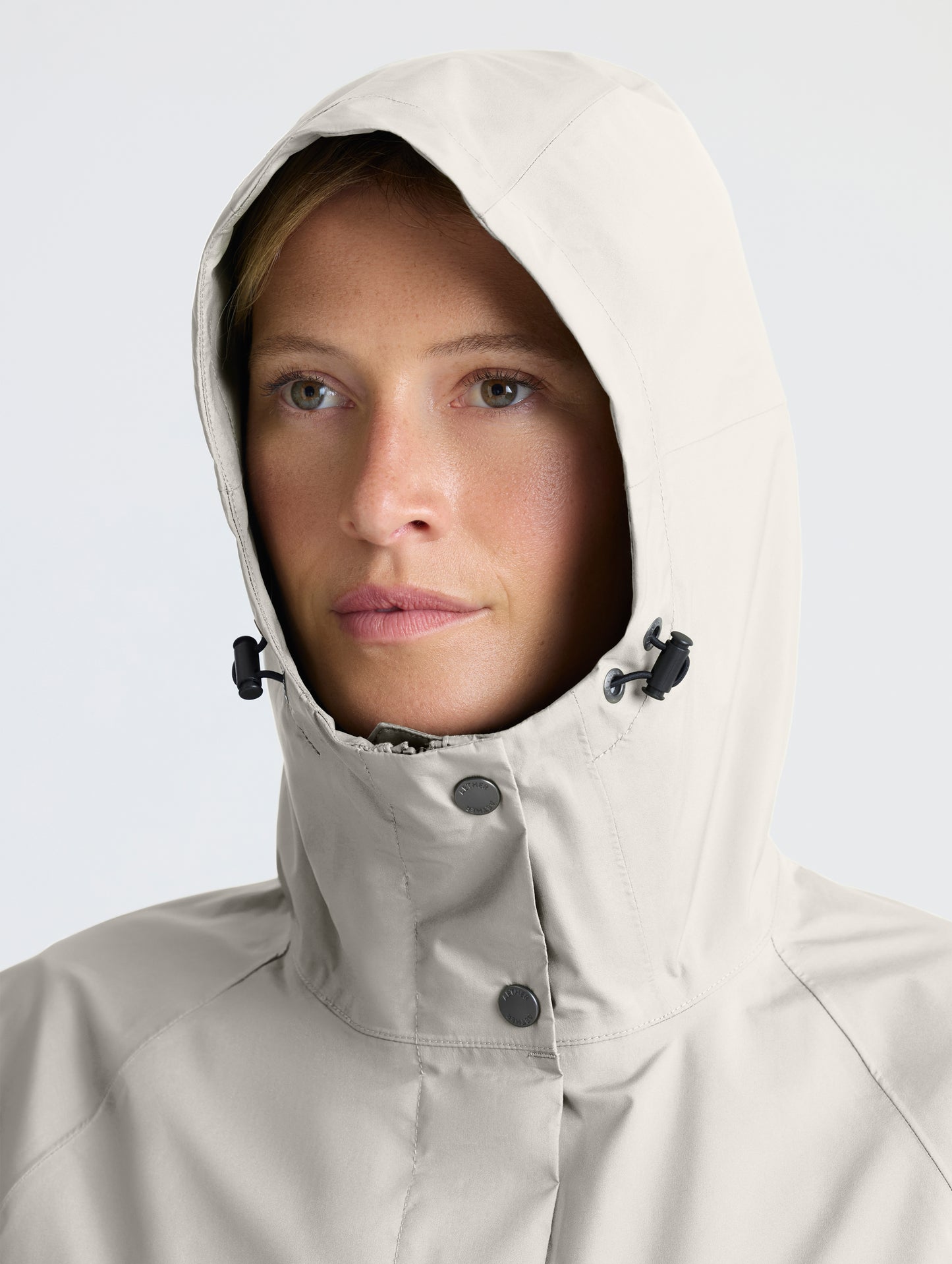 Closeup view of woman wearing hood of Storm All-Weather Jacket in Bone white from AETHER Apparel.