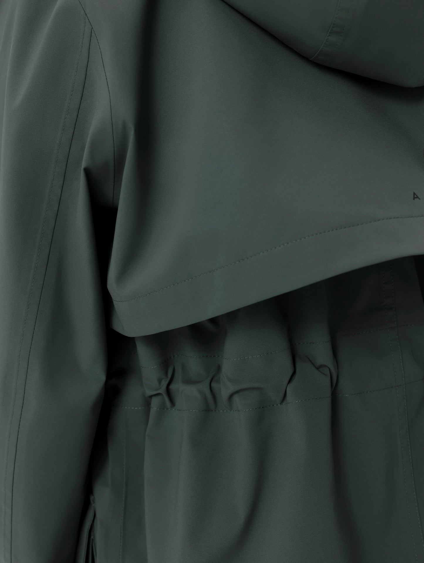 Closeup detailed view of the storm flap and cinching waist on the women's Wallace Rain Parka in Saville Green from AETHER Apparel.