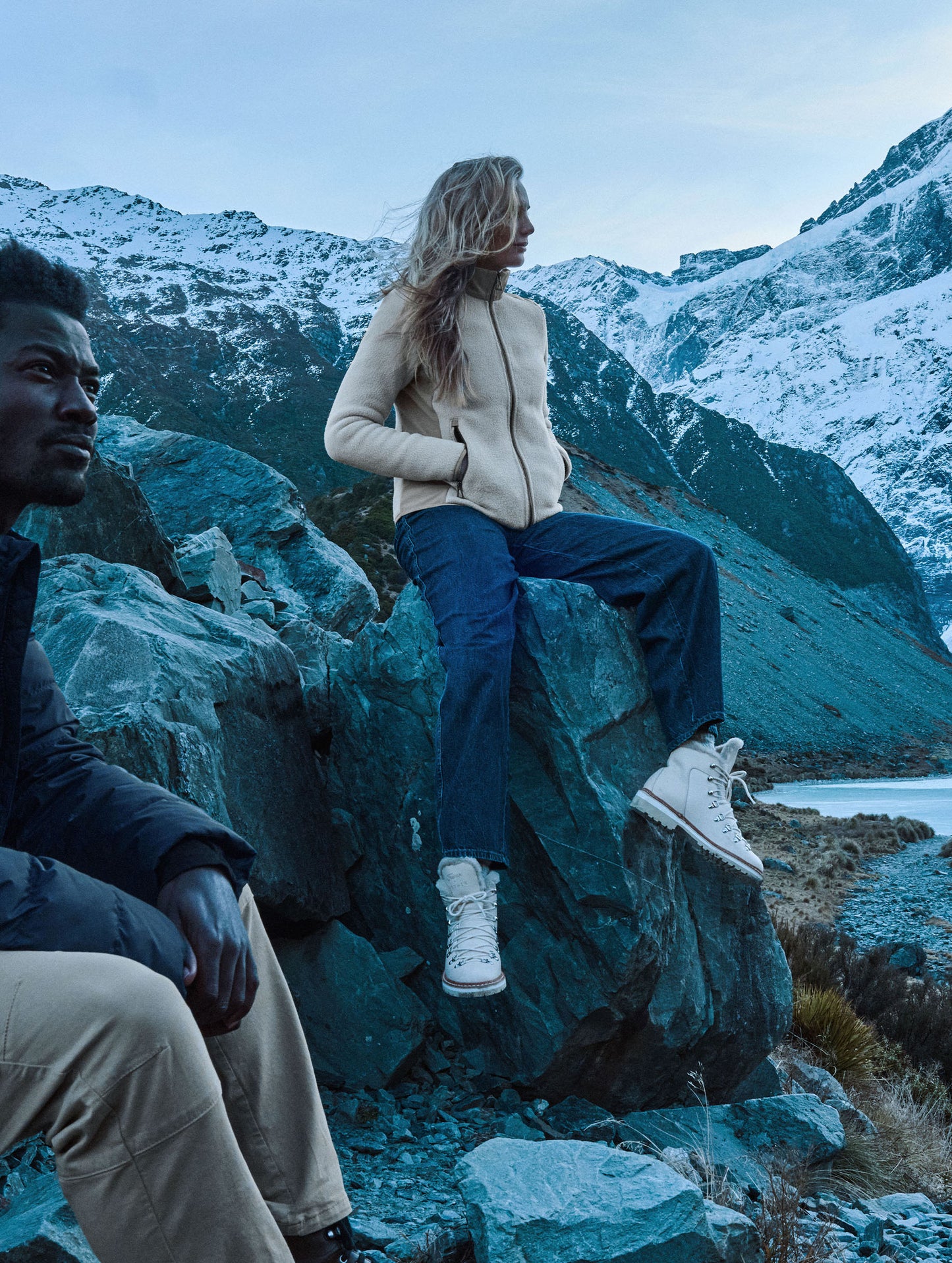 oman sitting on a boulder on the side of a mountain wearing the Walsh Full-Zip 2.0 in Bone and Desert Tan from AETHER Apparel.