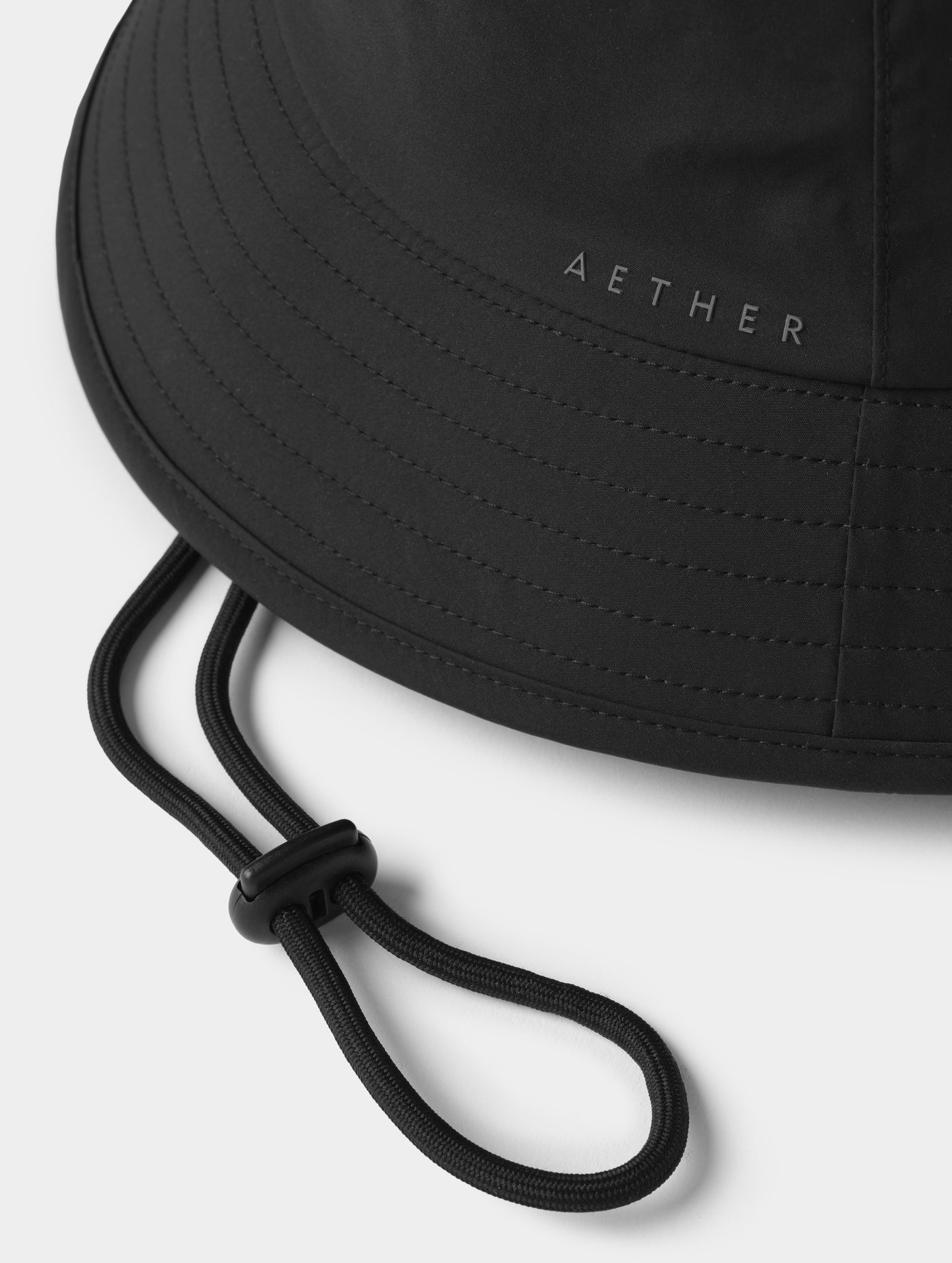 Closeup detailed view of the 5mm drawcord, cord lock, and silicone AETHER logo on the side of the Wallace Bucket Hat in Onyx Black from AETHER Apparel.