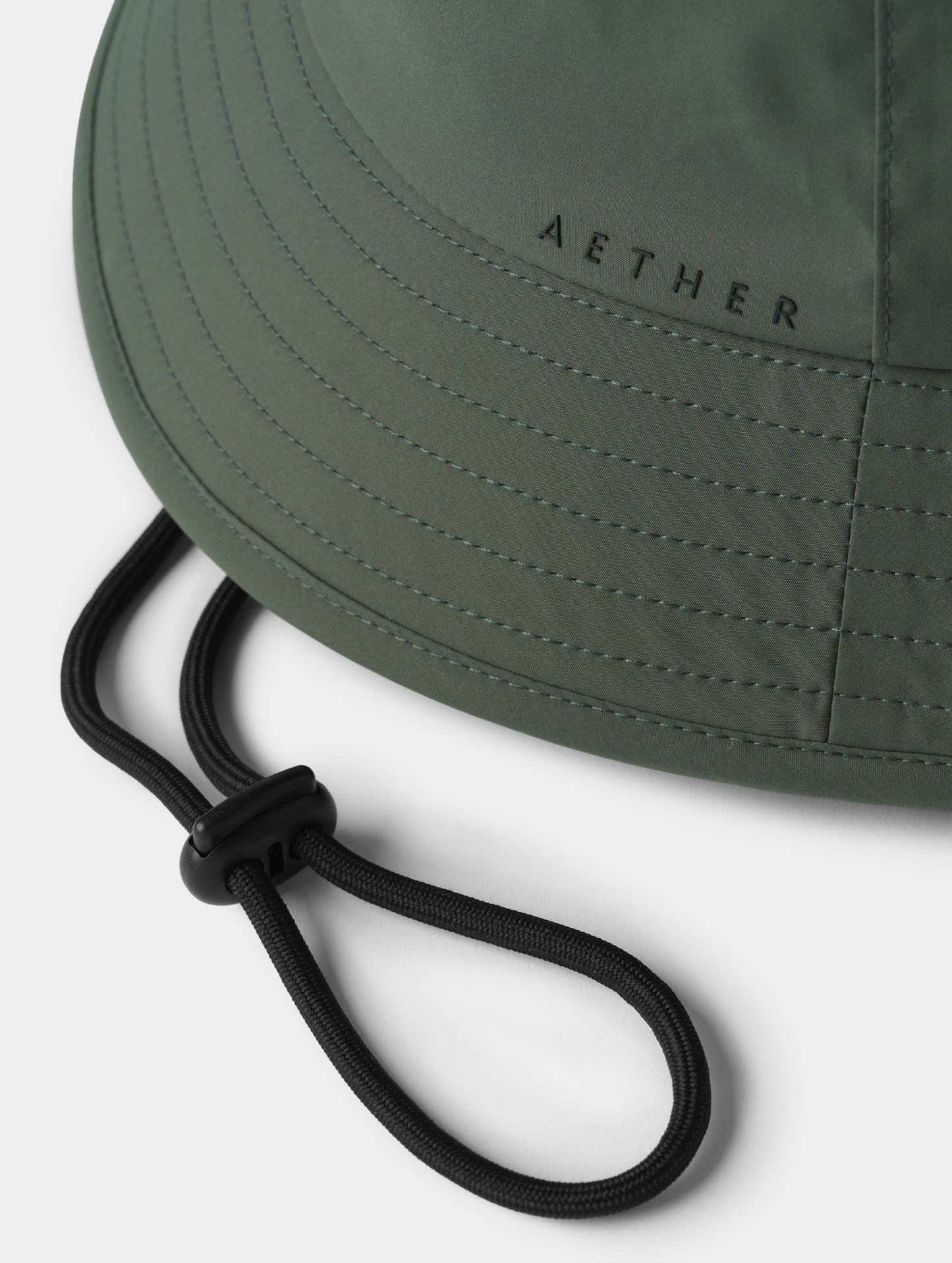Closeup detailed view of the 5mm drawcord, cord lock, and silicone AETHER logo on the side of the Wallace Bucket Hat in Saville Green from AETHER Apparel.