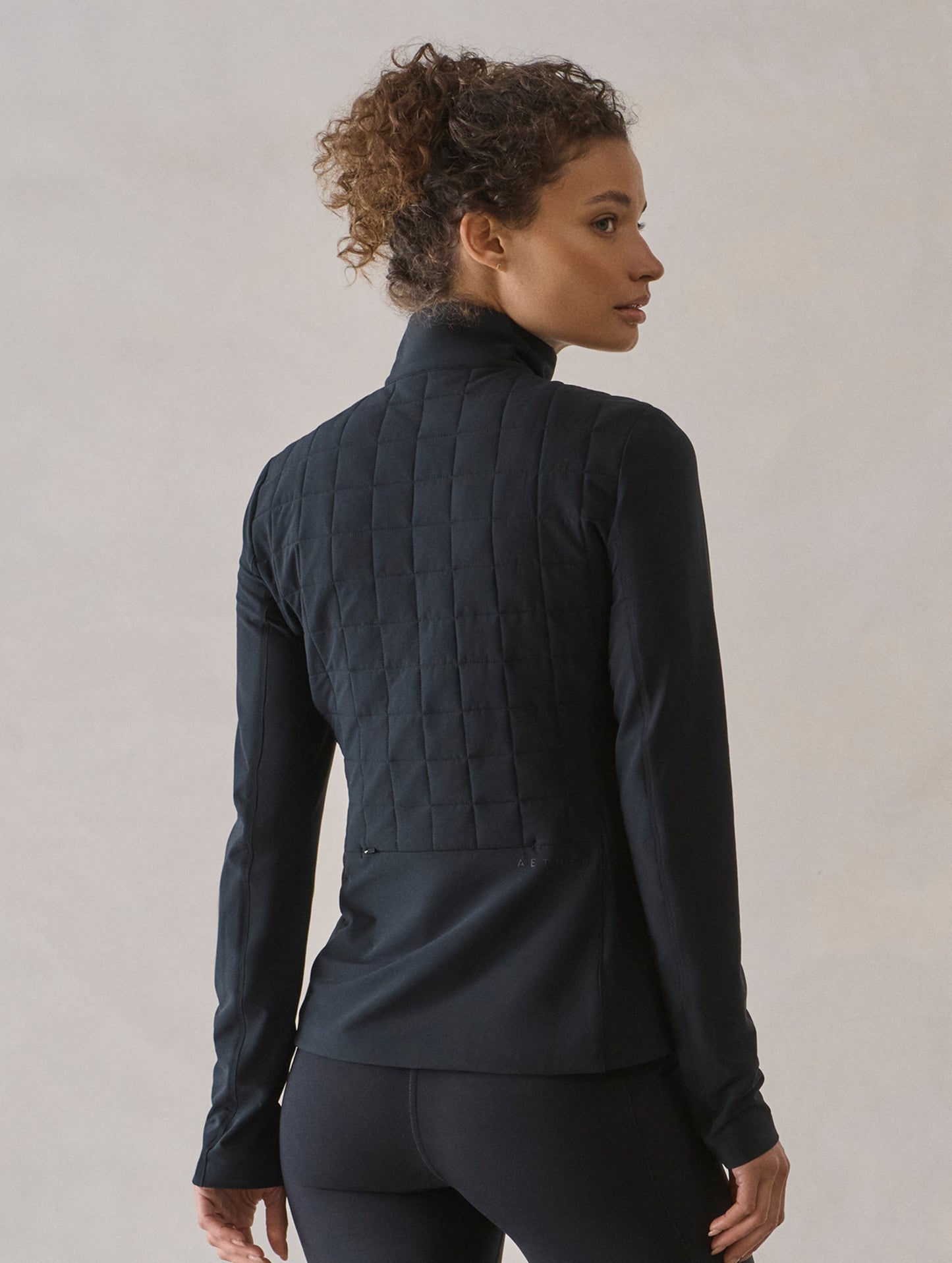 Rear 3/4 body view of woman wearing Wren Insulated Half-Zip in Onyx Black from AETHER Apparel.