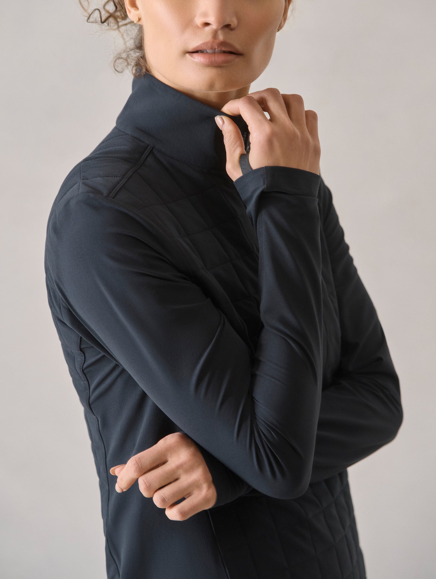 Closeup view of woman with folded arms wearing the Wren Insulated Half-Zip in Onyx Black from AETHER Apparel.