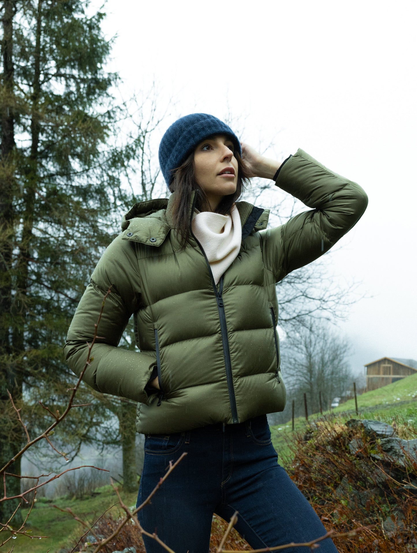Outdoor lifestyle image of woman standing on hill in front of trees and cabin wearing Avesta Cashmere Scarf in Winter White from AETHER Apparel.
