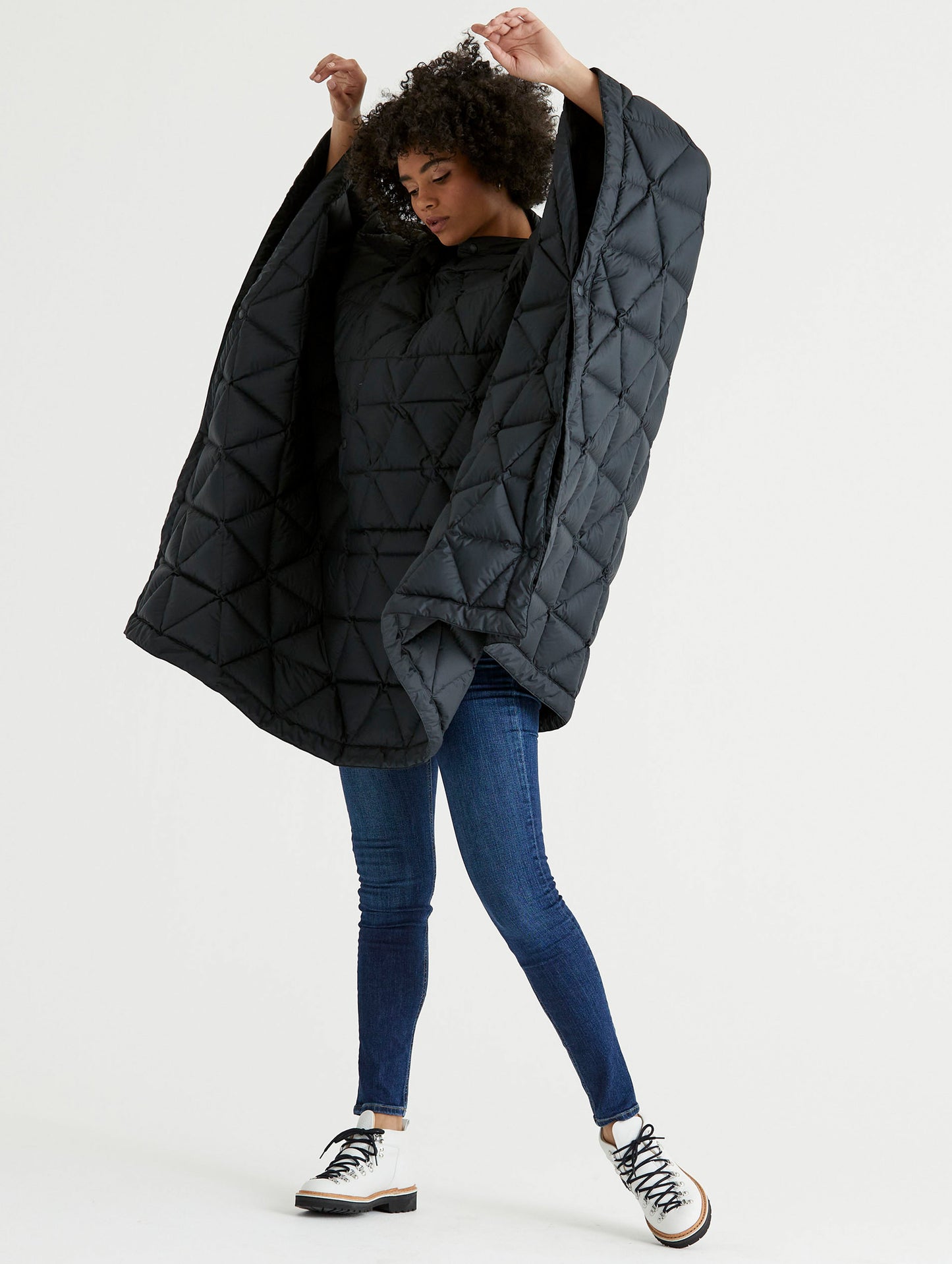 Front 3/4 full-body view of woman raising arms wearing Down Poncho in Onyx Black from AETHER Apparel.