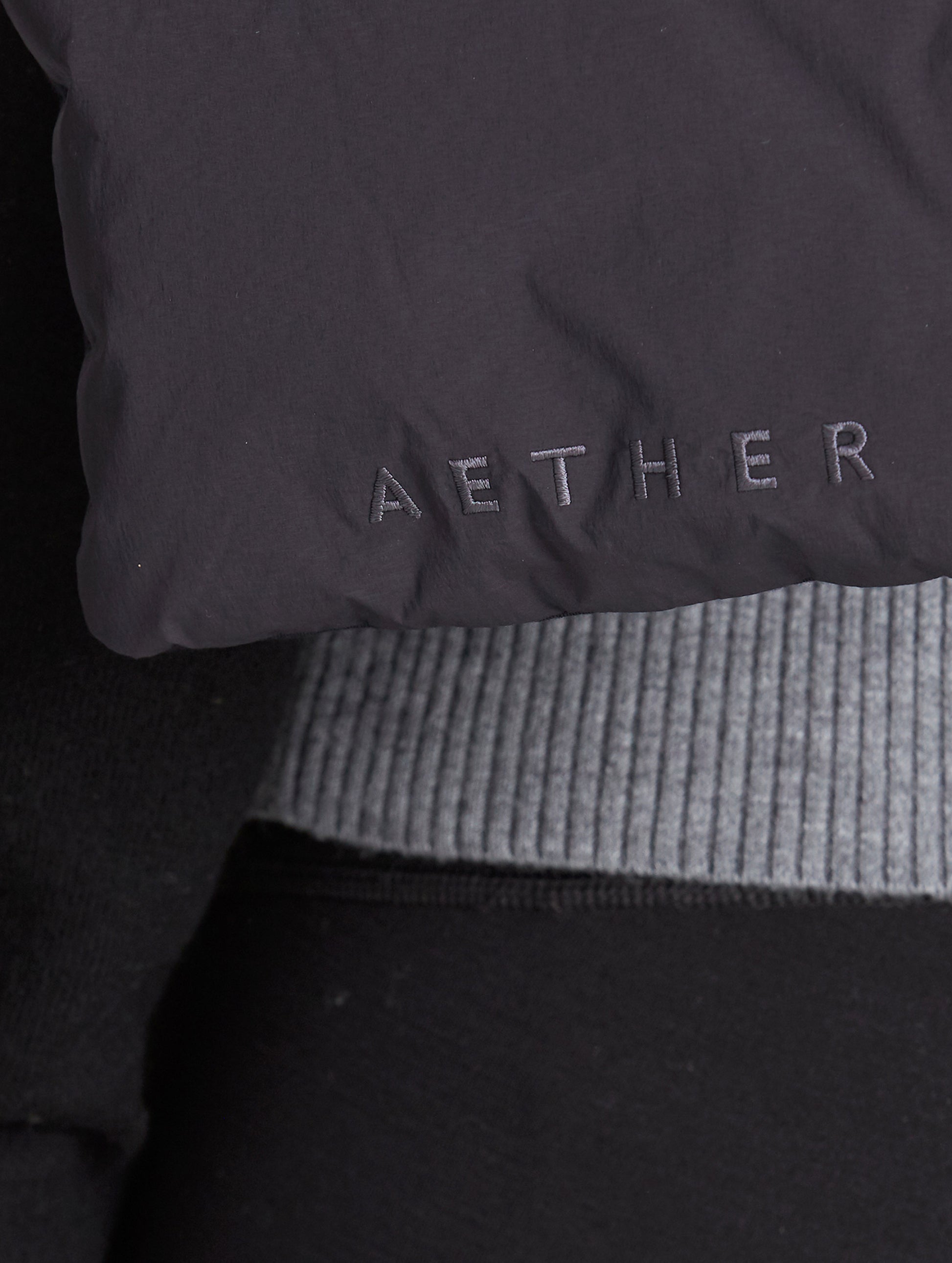 Closeup detailed view of AETHER logo on Quilted Down Scarf in Onyx Black from AETHER Apparel.