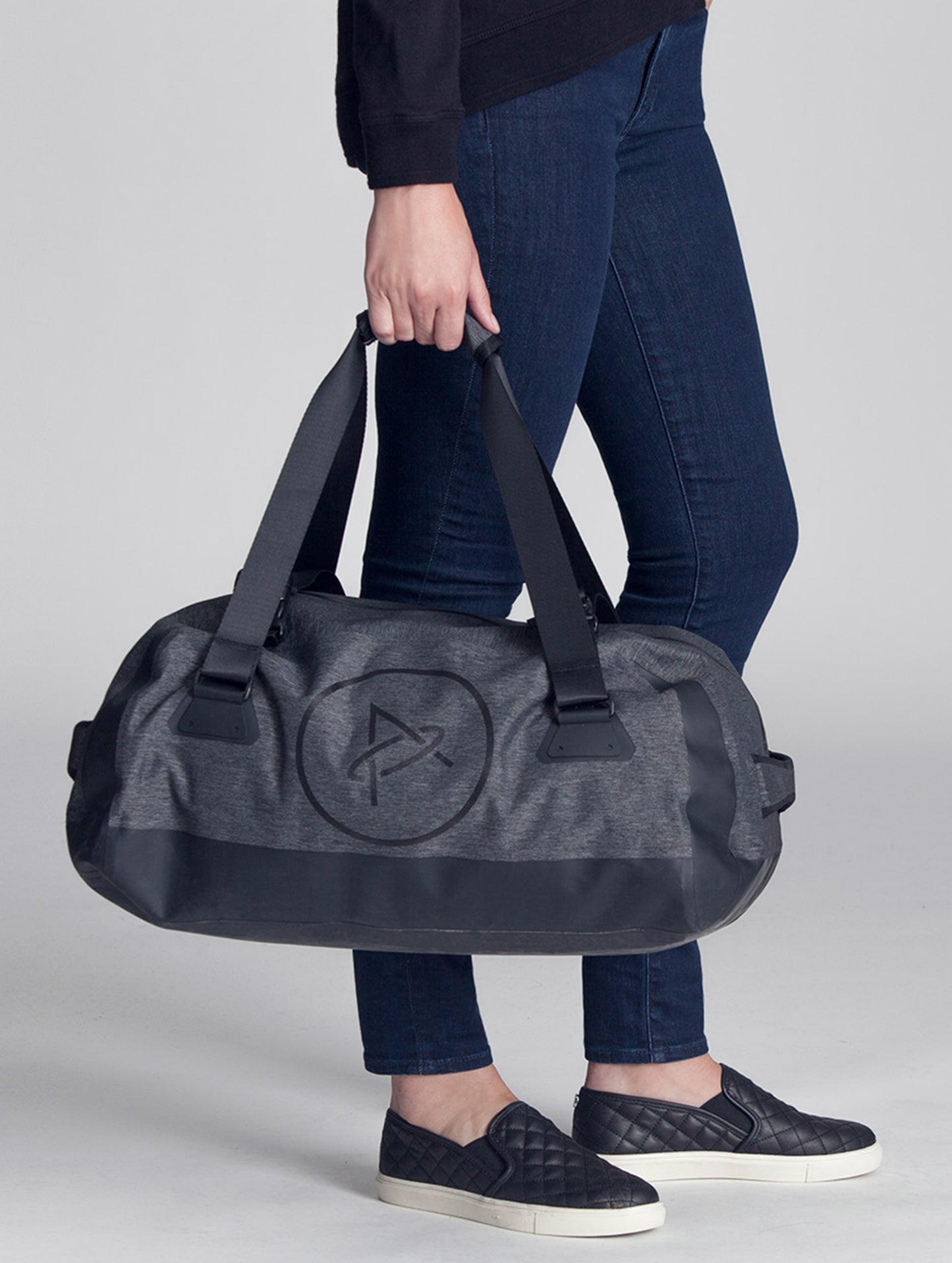 Closeup front angled view of woman carrying Welded Duffle Small in Charcoal Heather from AETHER Apparel.