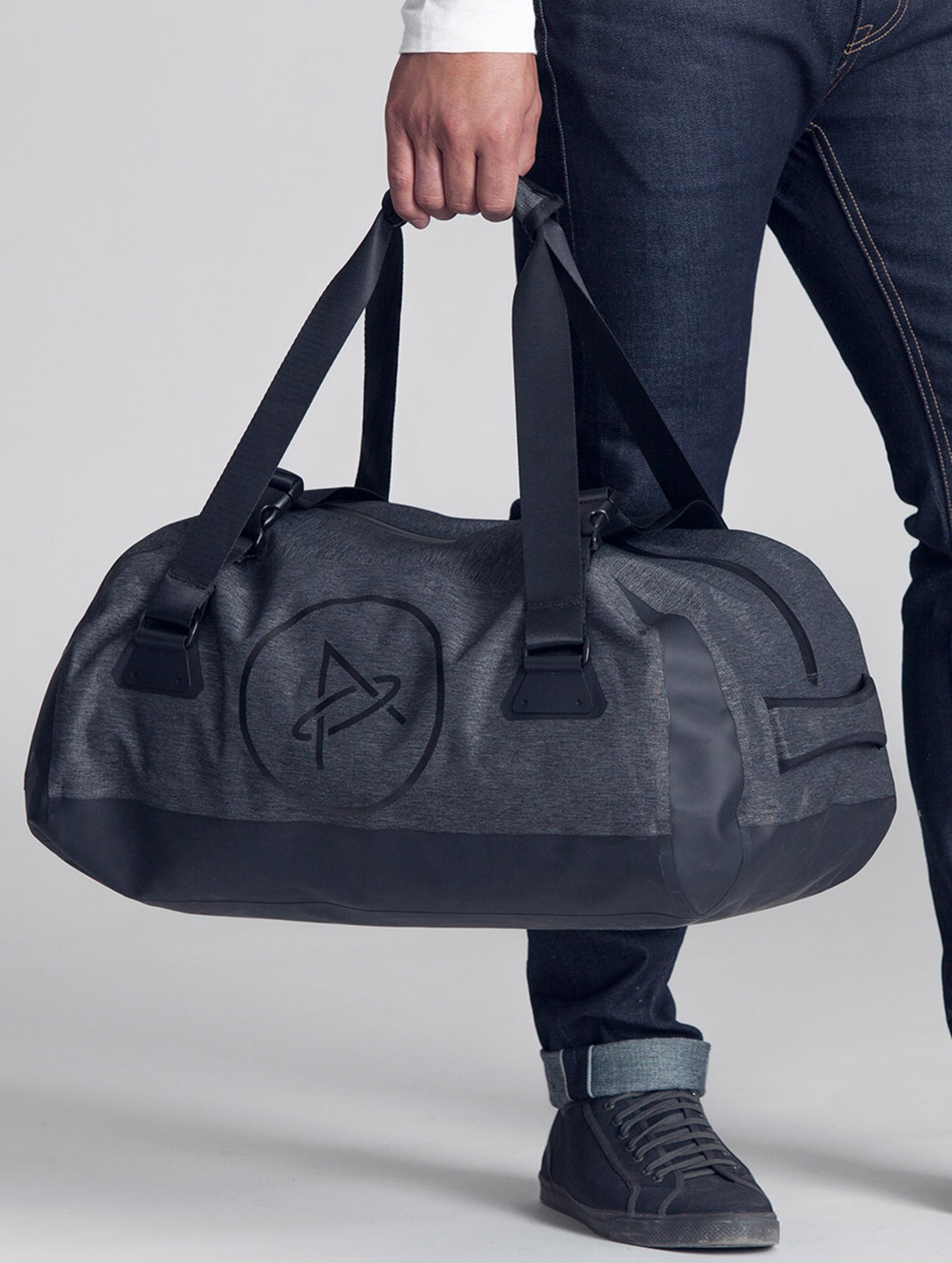 Closeup front angled view of man carrying Welded Duffle Small in Charcoal Heather from AETHER Apparel.