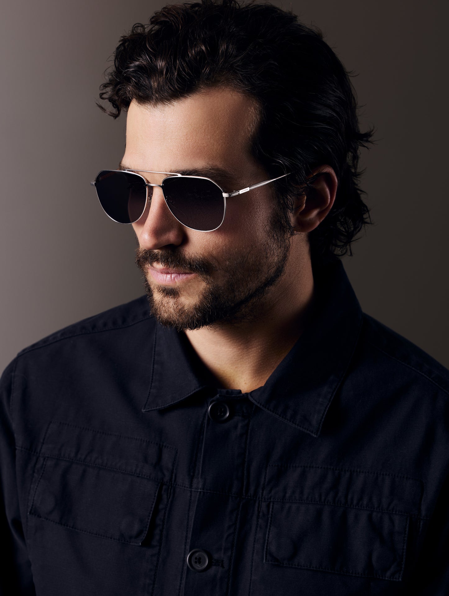 Front left 3/4 view of man wearing Bryce Sunglass in Brushed Silver titanium with Grey Lens from AETHER Apparel.