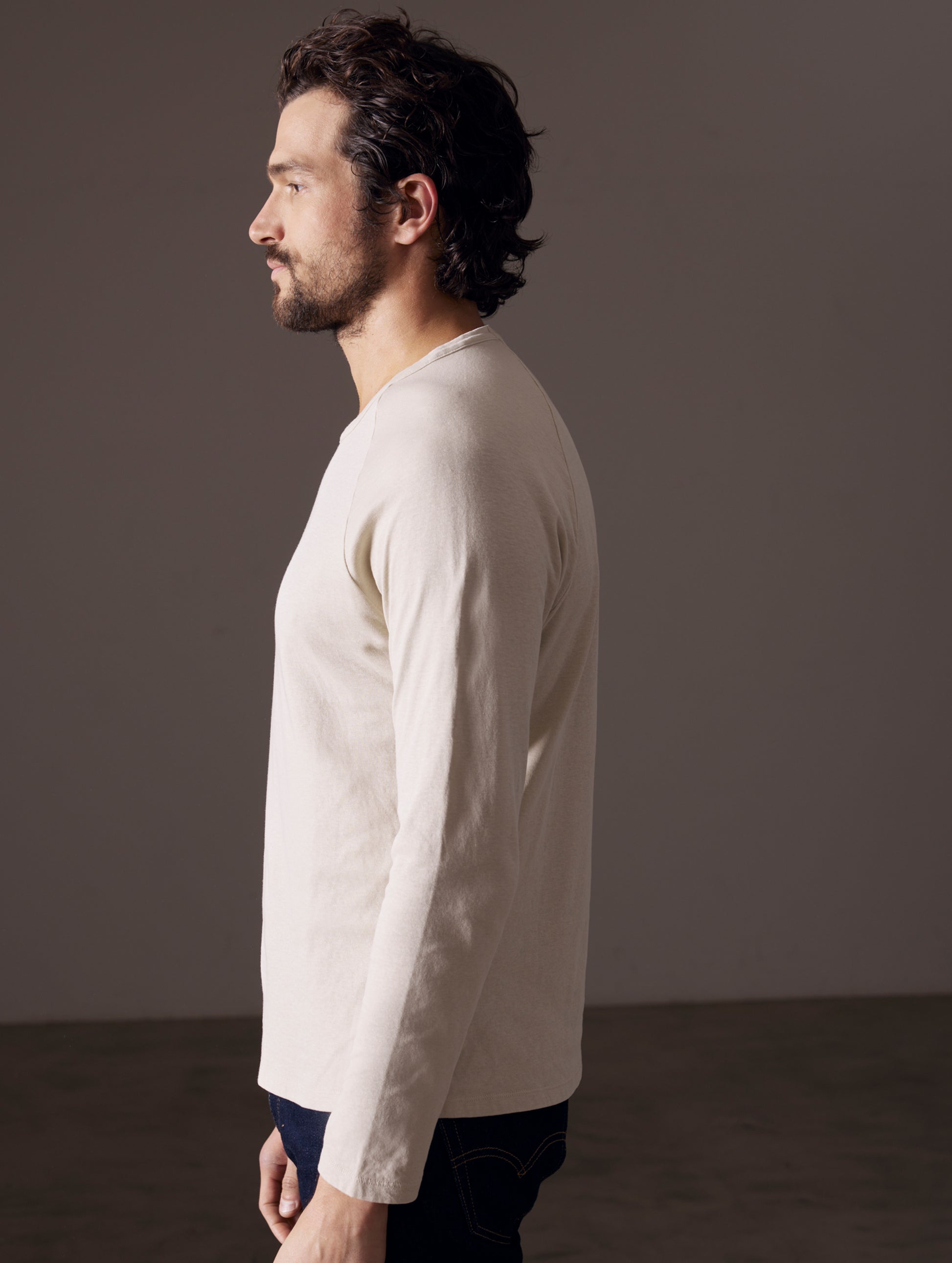 Side profile body view of man wearing Buckhorn Cotton Raglan Long-Sleeve Tee in Bone white from AETHER Apparel.