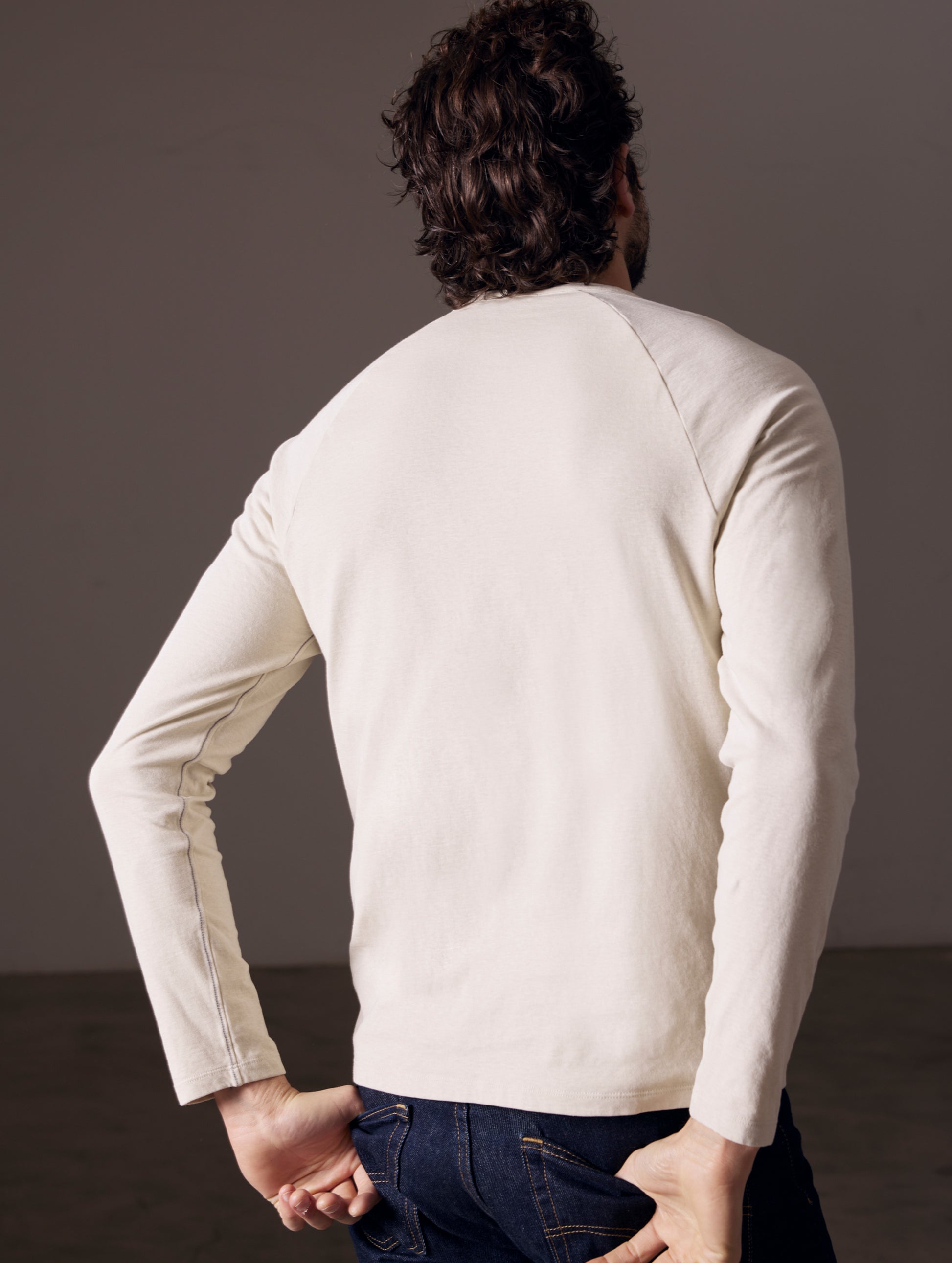 Rear angled body view of man wearing Buckhorn Cotton Raglan Long-Sleeve Tee in Bone white from AETHER Apparel.