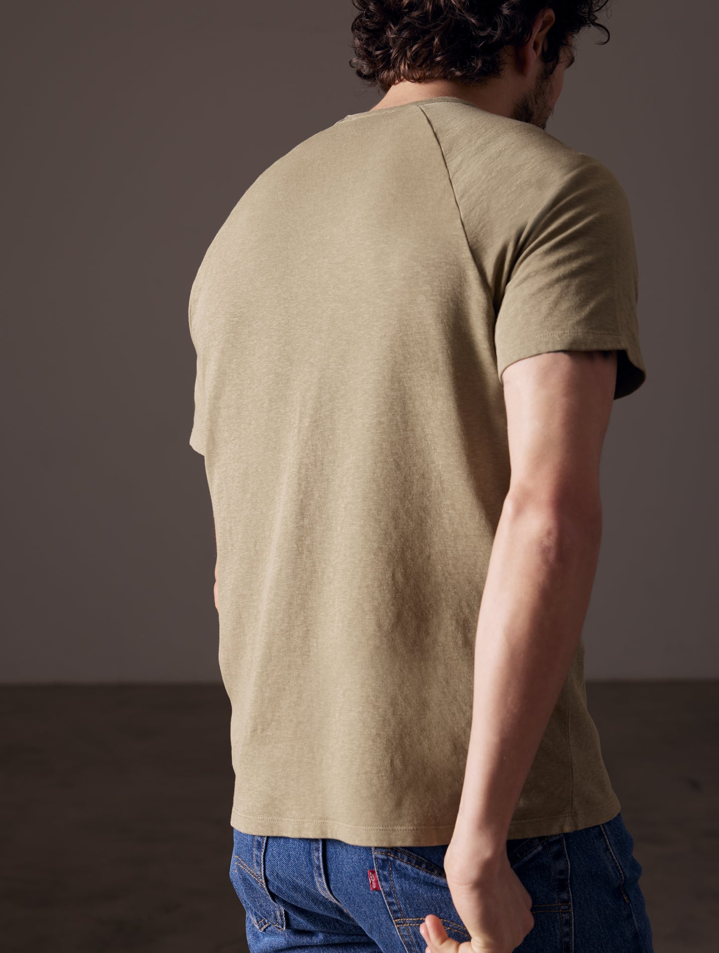 Rear angled body view of man wearing Buckhorn Cotton Raglan Tee in Mineral Green from AETHER Apparel.