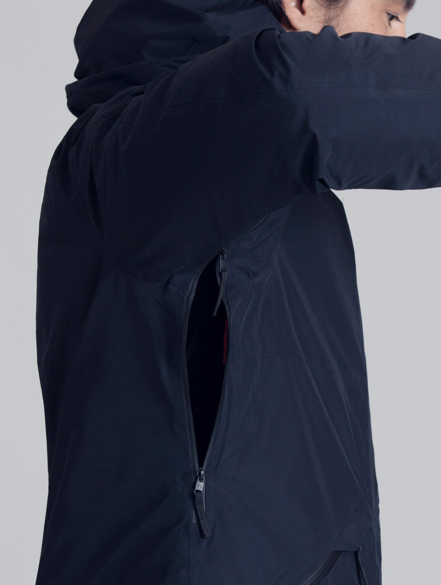 Man wearing black Crest Down Jacket from AETHER Apparel, displaying zippered underarm ventilation.