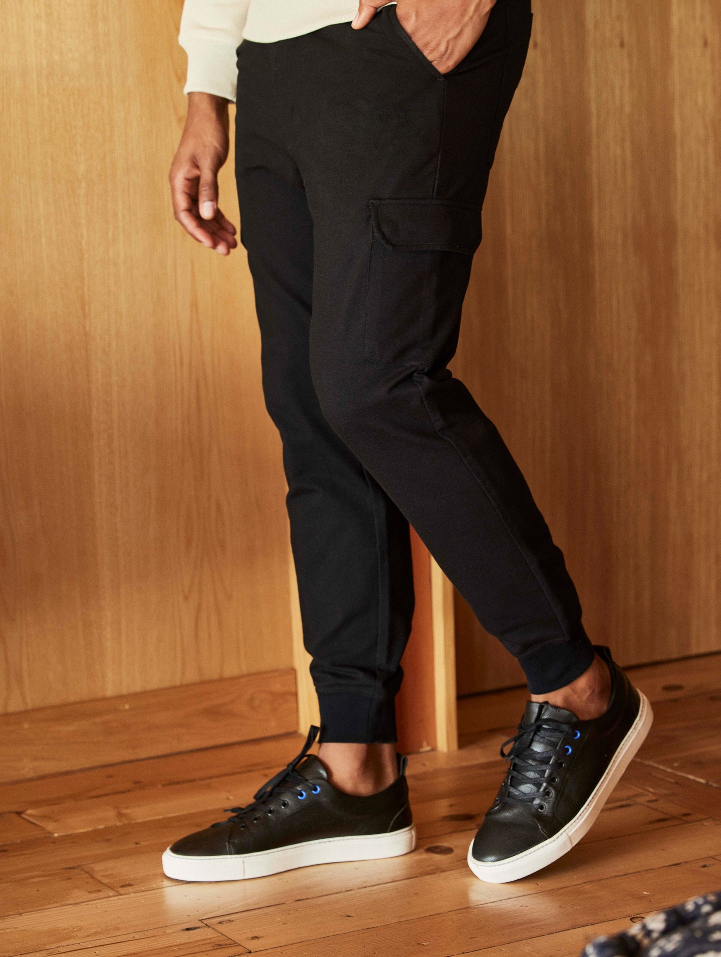 Lifestyle image of man standing on wood floor wearing Dalton Low-Top Sneaker in Onyx Black from AETHER Apparel.