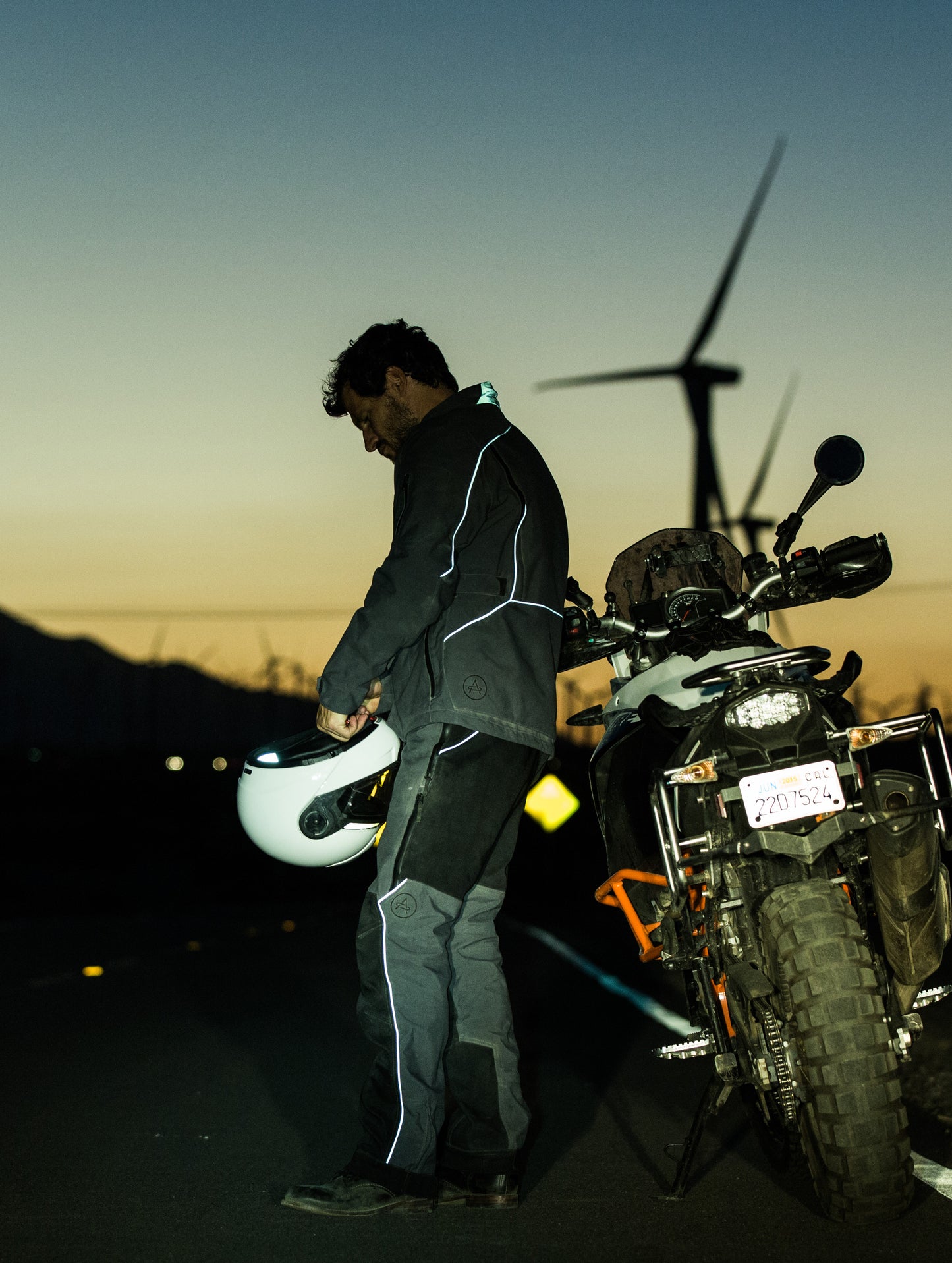 Man beside motorcycle outdoors wearing grey Expedition Motorcycle Jacket from AETHER Apparel.