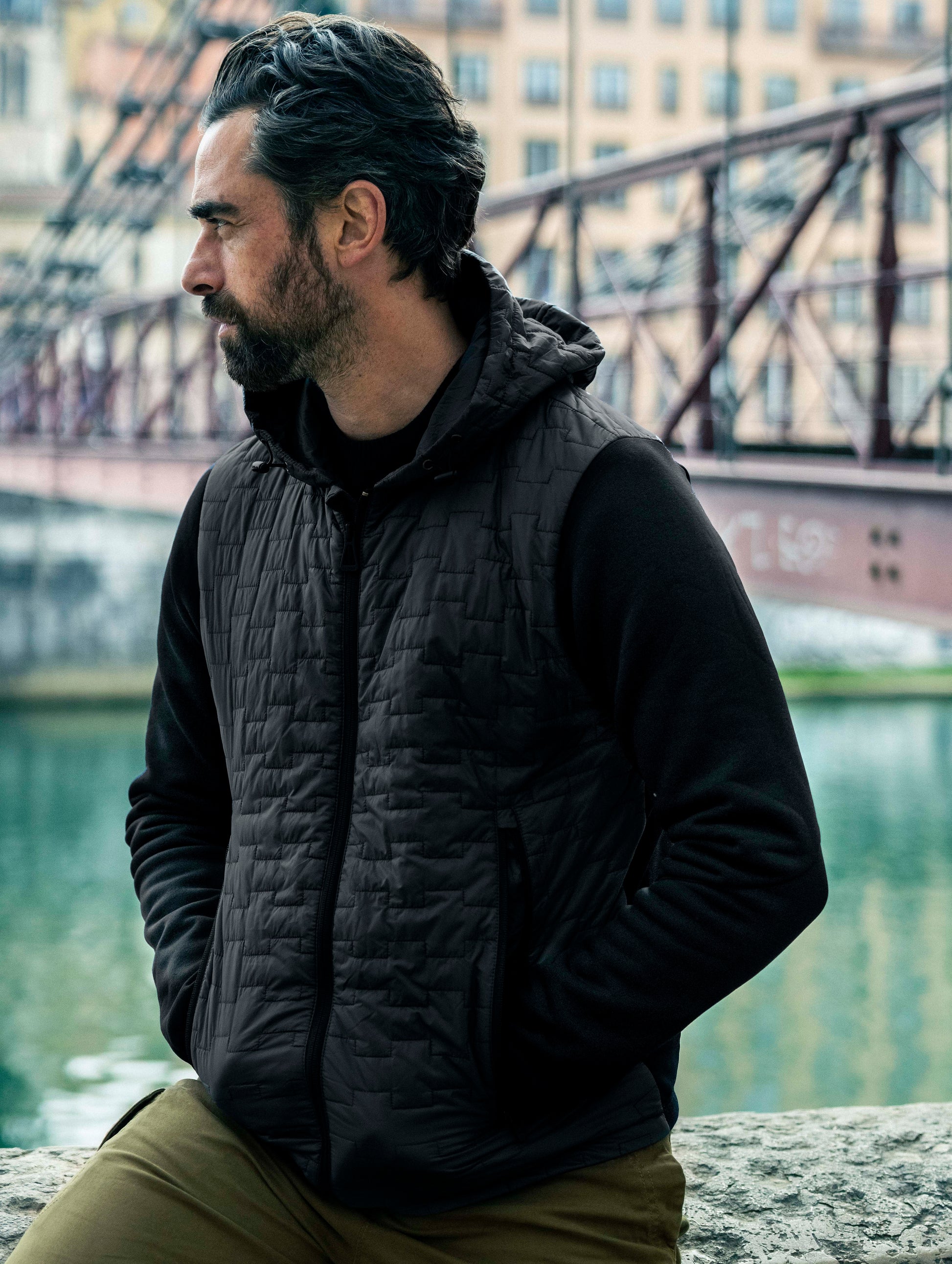 Man sitting outdoors wearing insulated Hybrid Tech Hoodie from AETHER Apparel.