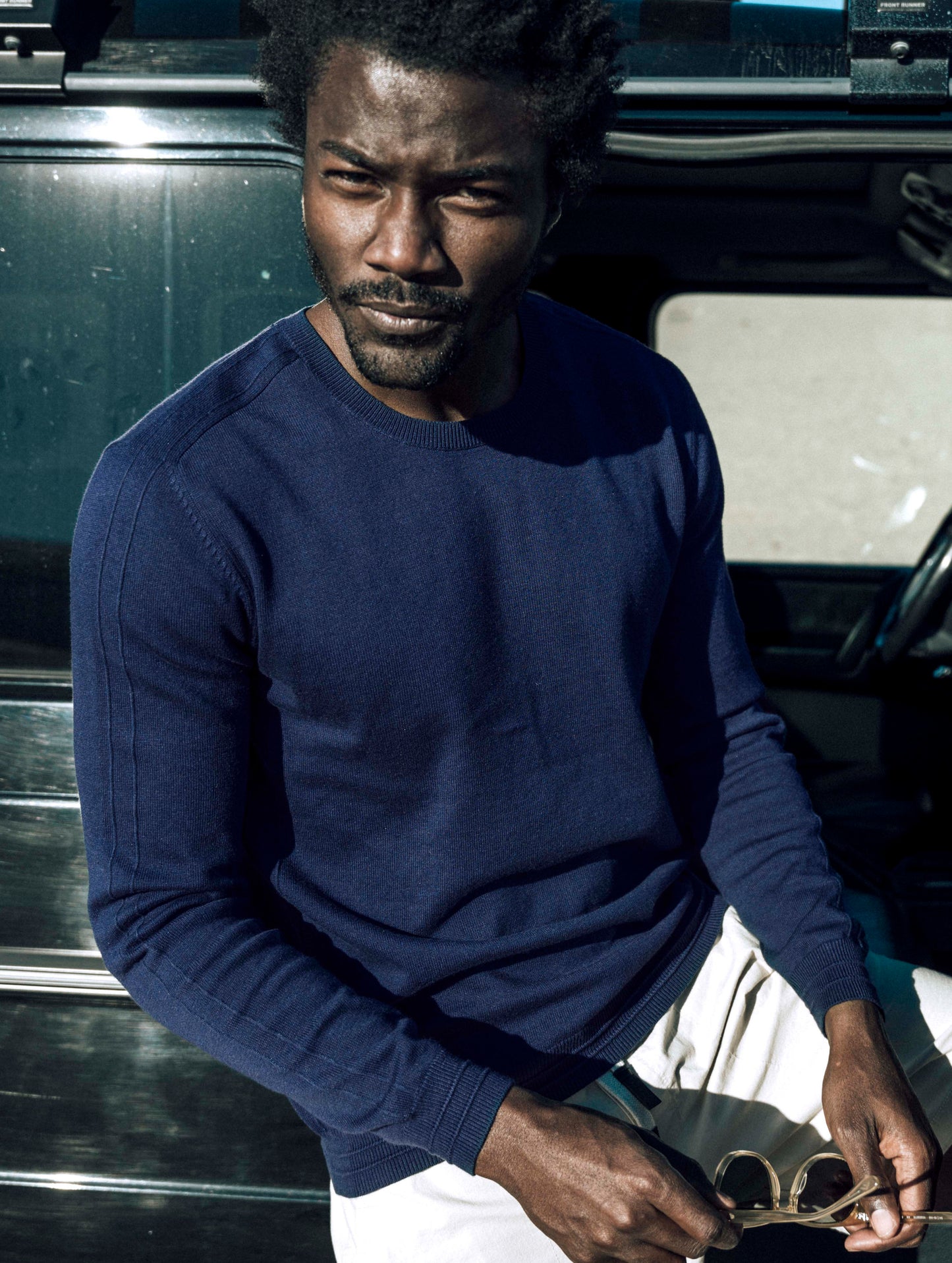 Outdoor lifestyle image of man leaning against SUV wearing Irving Sweater in Total Eclipse dark blue from AETHER Apparel.