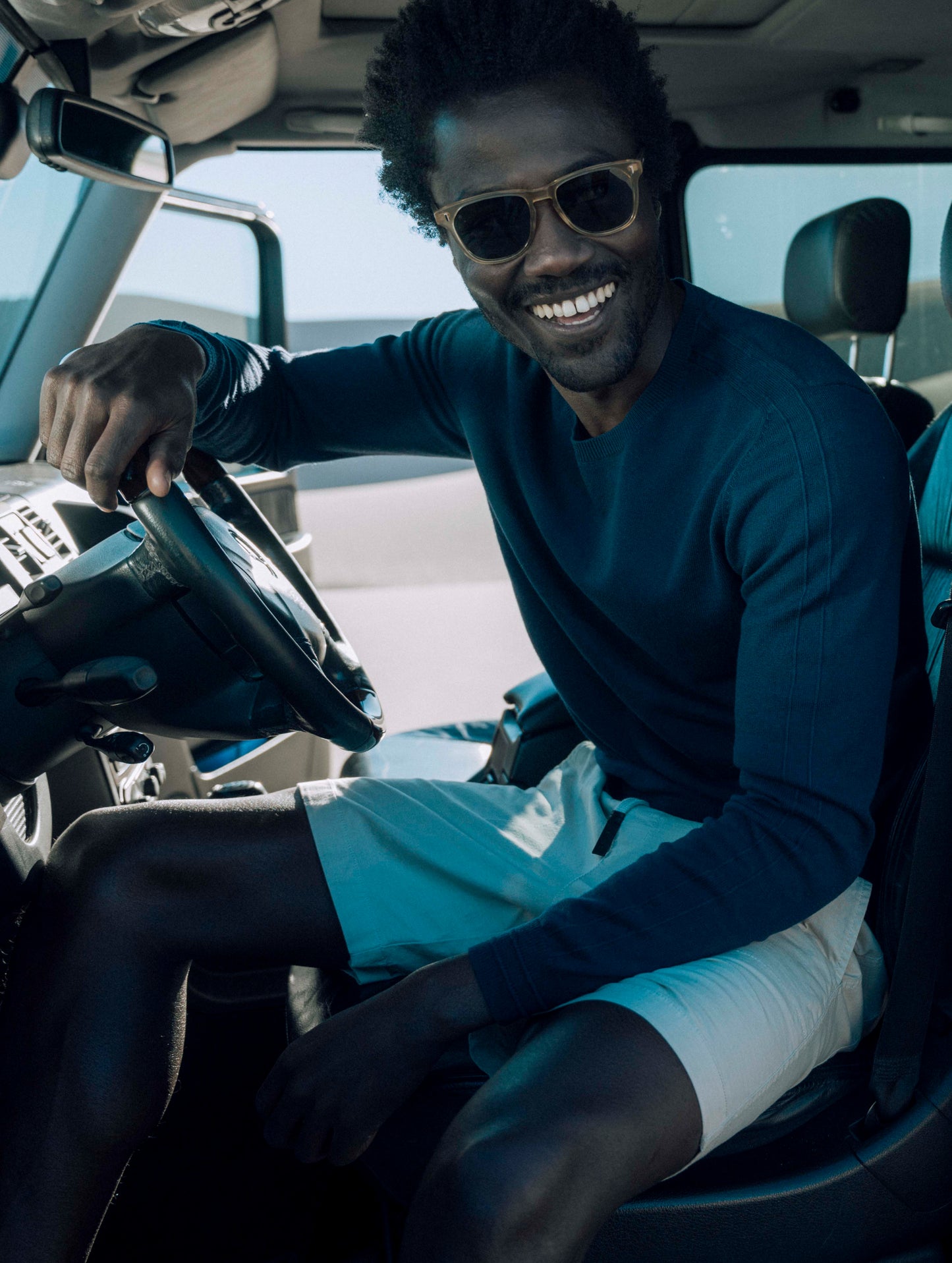 Outdoor lifestyle image of man sitting behind steering wheel in SUV wearing Irving Sweater in Total Eclipse dark blue from AETHER Apparel.