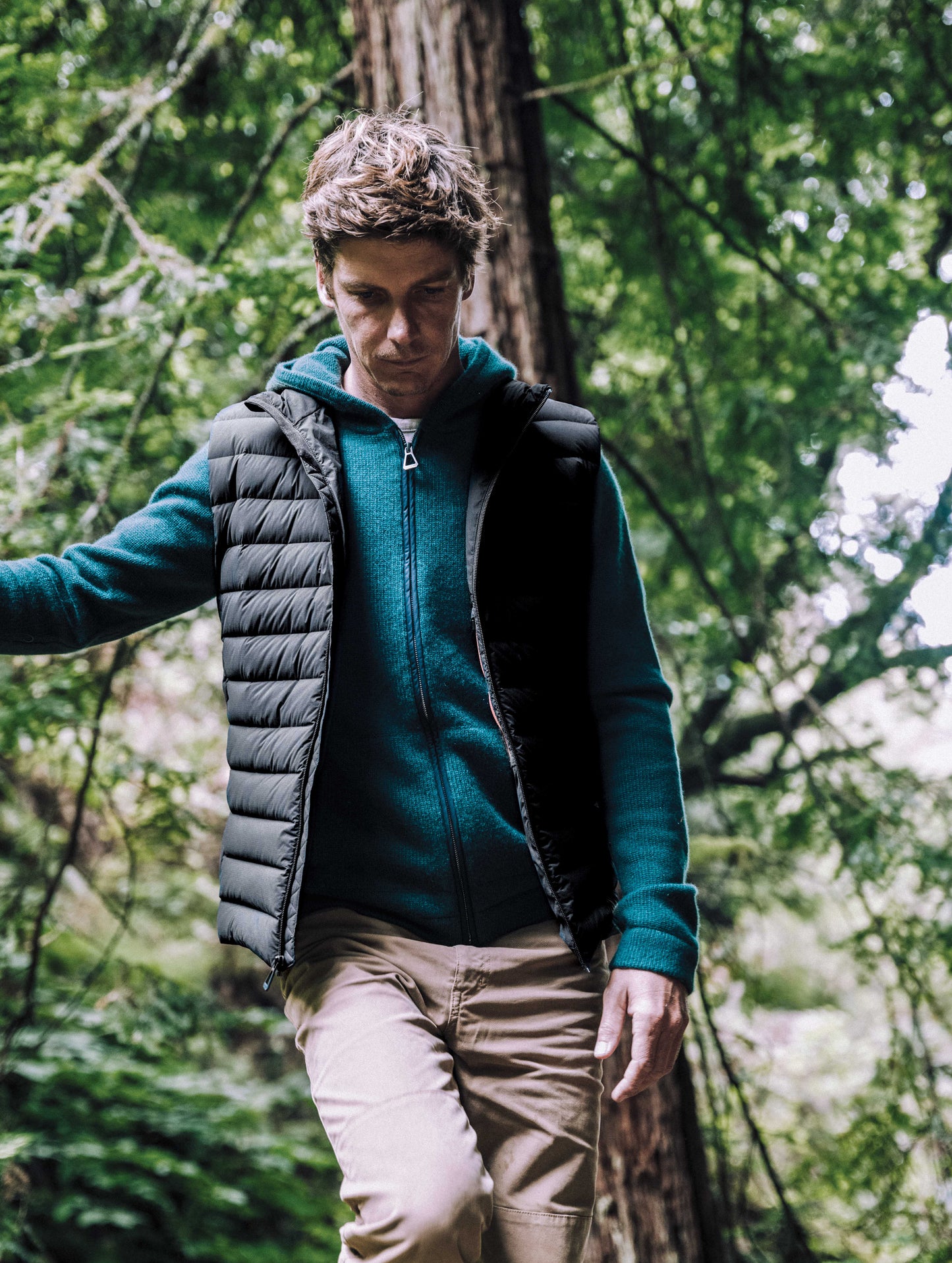Outdoor lifestyle image of man walking through woods wearing Launch Vest in Onyx Black from AETHER Apparel.