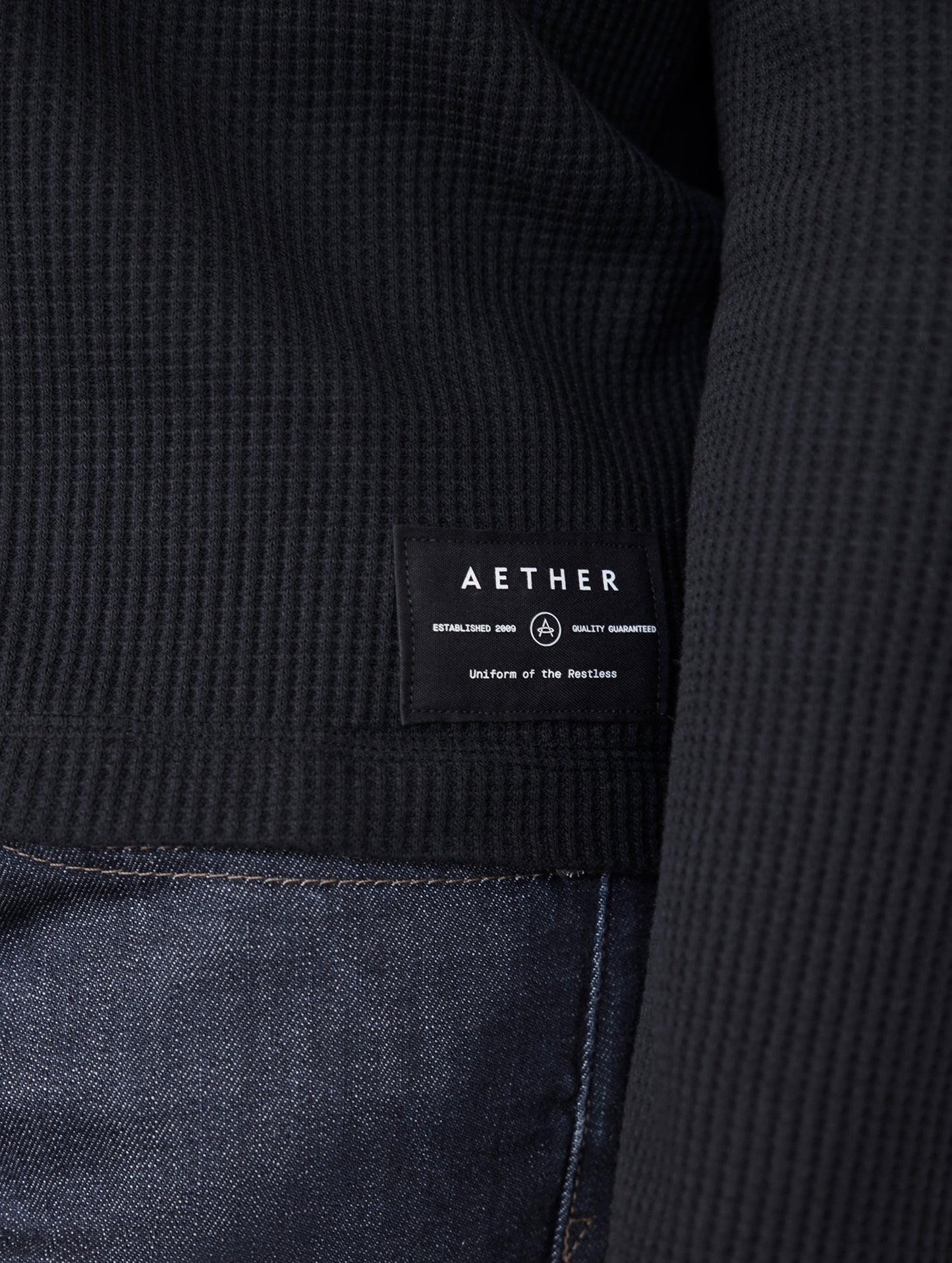 black long sleeve henley with small AETHER logo patch on bottom left