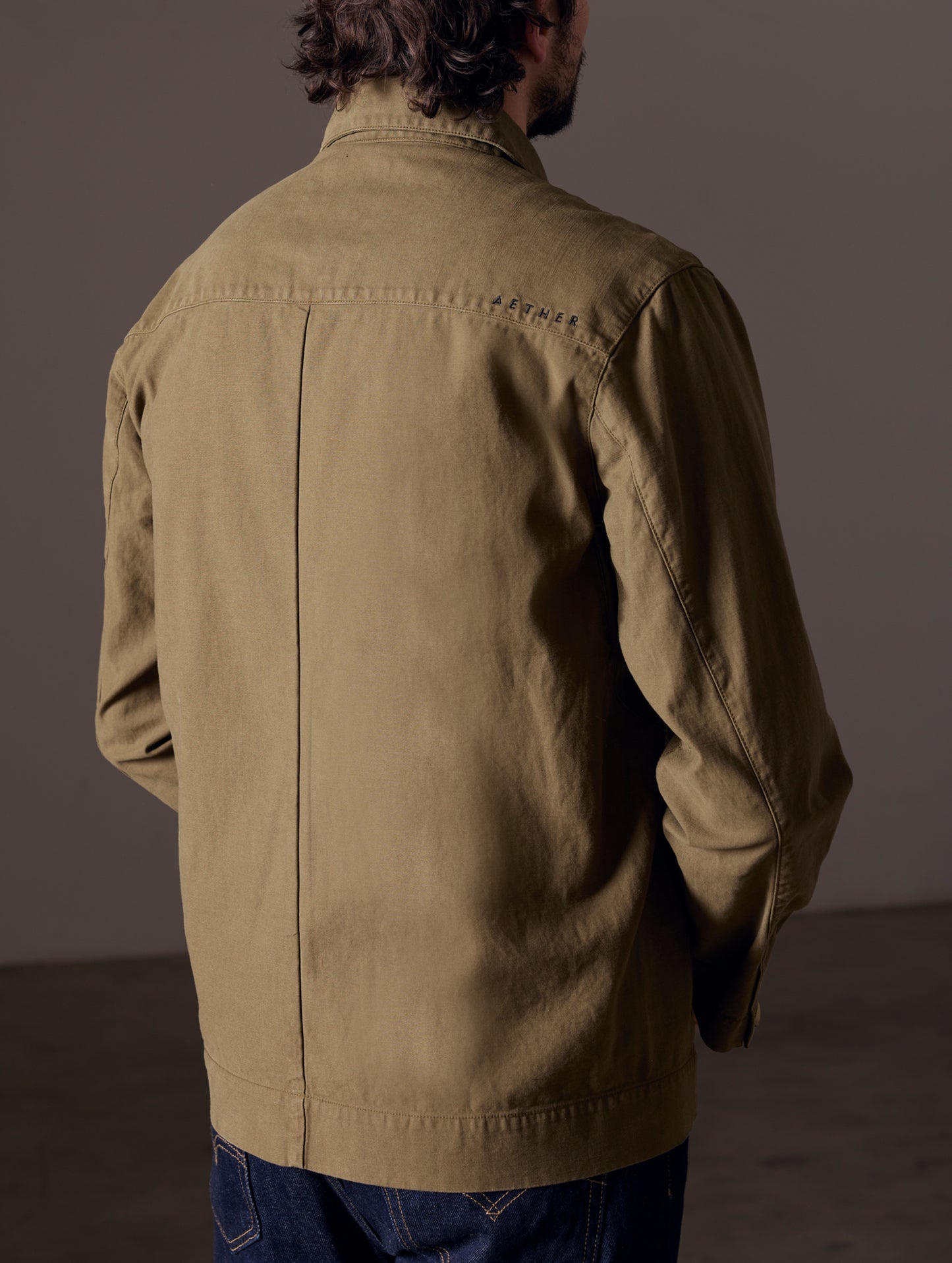 Rear 3/4 body view of man wearing Mesa Jacket in Command Green from AETHER Apparel.
