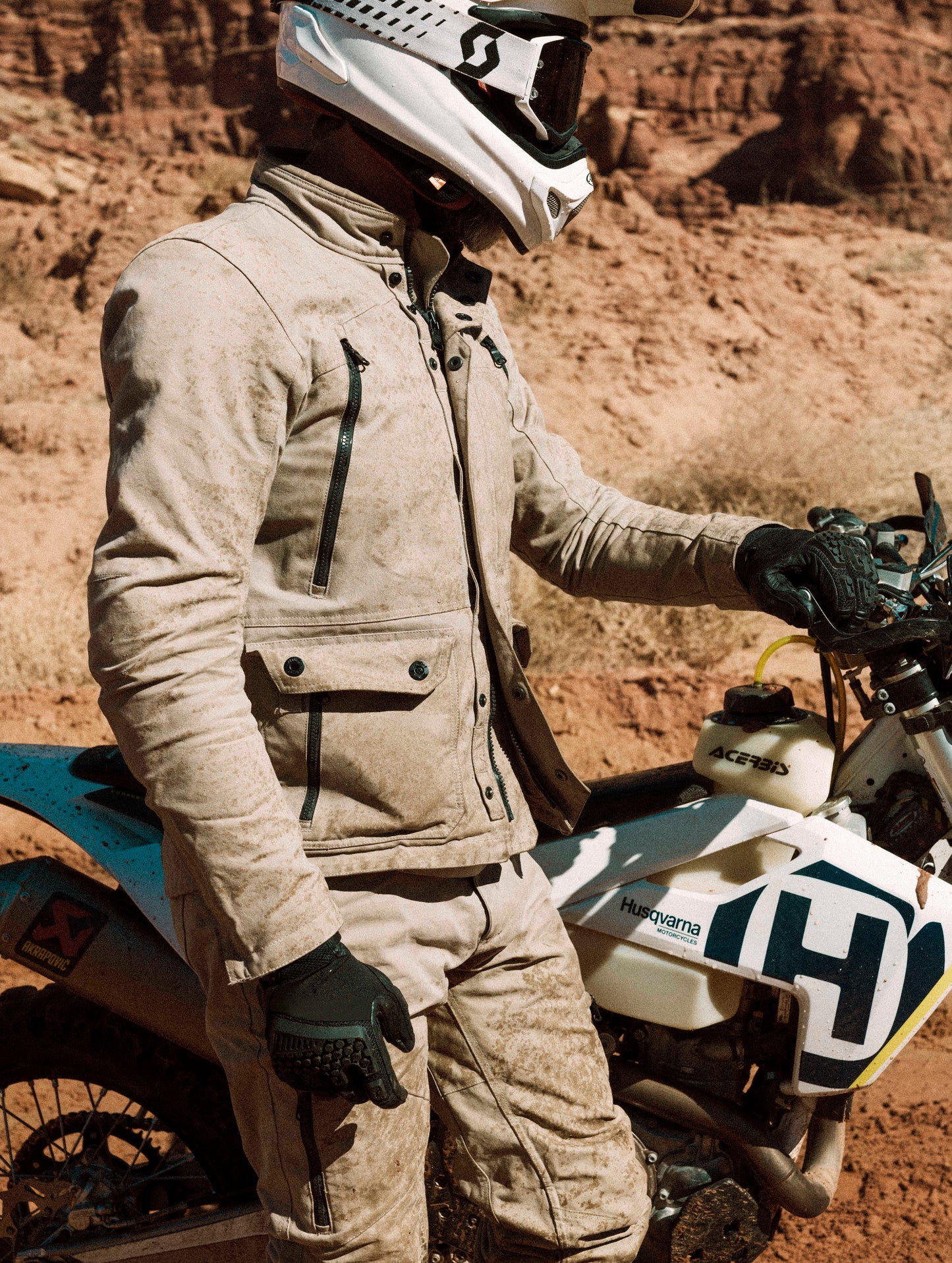 Outdoor lifestyle image of man standing next to enduro motorcycle wearing Mojave Motorcycle Jacket in Dark Sand from AETHER Apparel.