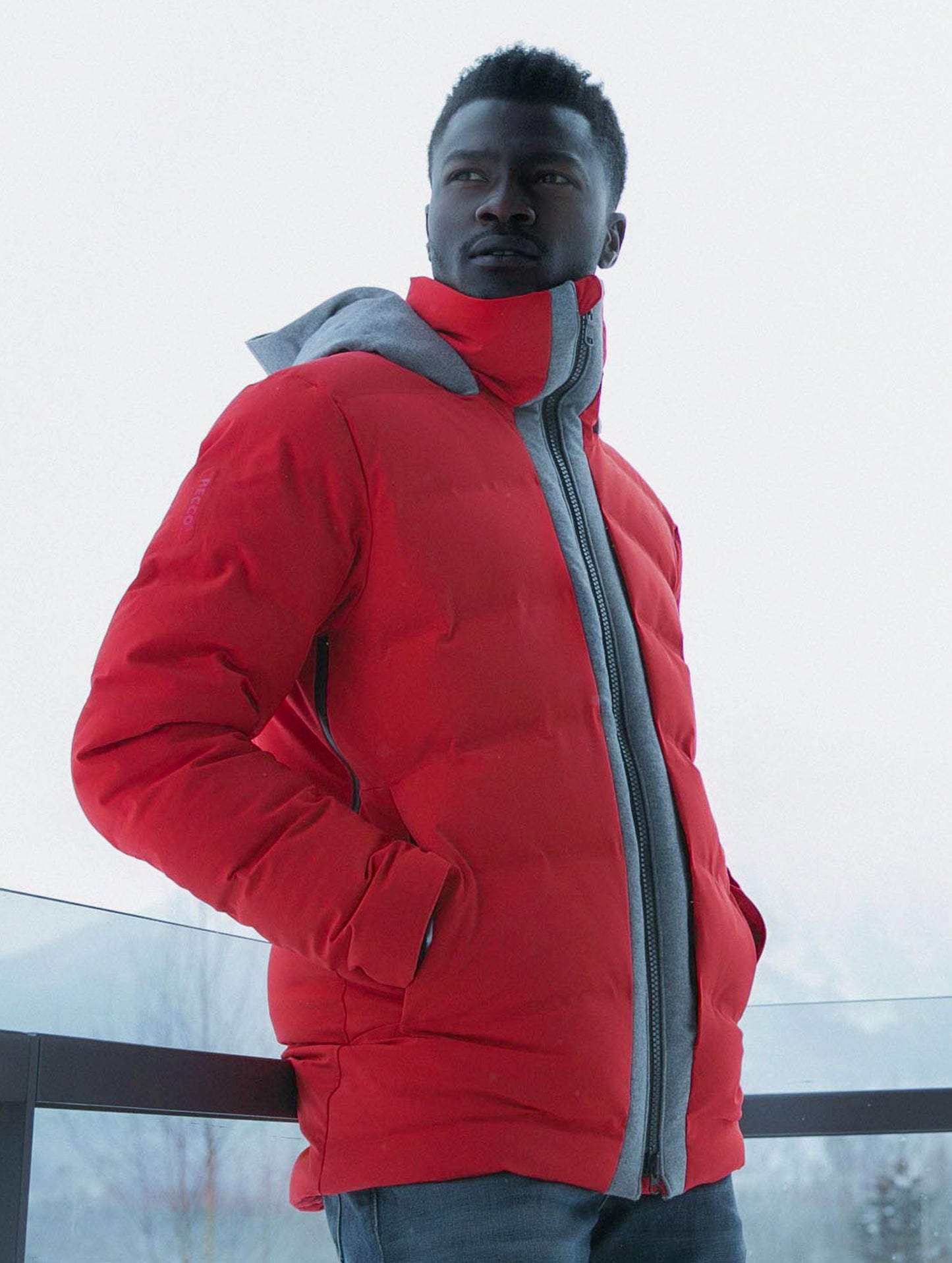Outdoor lifestyle shot of man standing against railing wearing Nordic Jacket in Racing Red from AETHER Apparel.