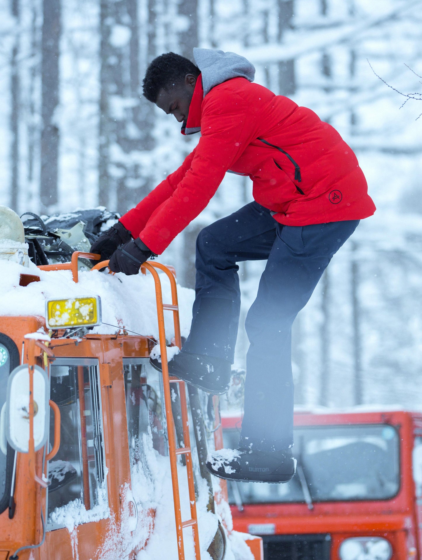 Outdor lifestyle image of man climbing up snow cat roof ladder wearing Nordic Jacket in Racing Red from AETHER Apparel.
