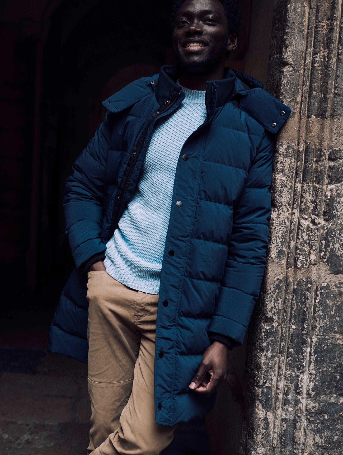 Outdoor lifestyle image of man leaning against wall wearing Scott Parka in Nordic Navy blue from AETHER Apparel.