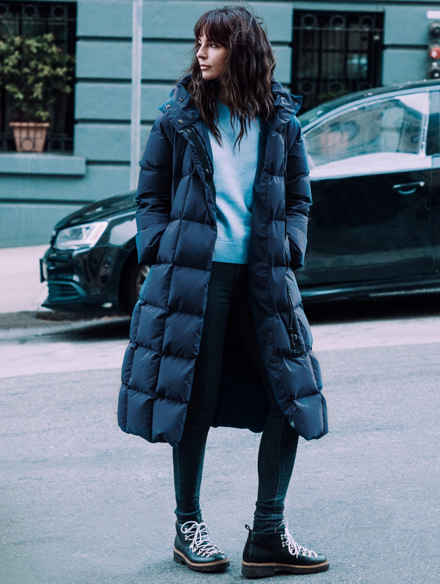 Outdoor lifestyle image of woman standing on hilly city street wearing Shaw Jacket in Nordic Navy Blue from AETHER Apparel.