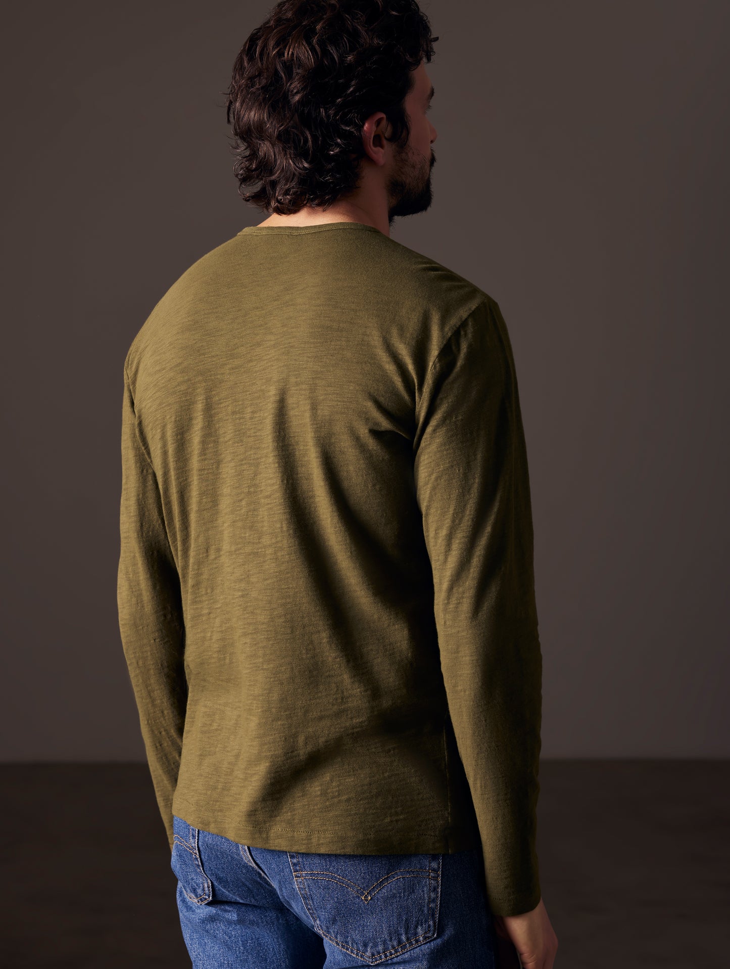 Rear angled body view of man wearing Slub Long-Sleeve Tee in Command Green from AETHER Apparel.