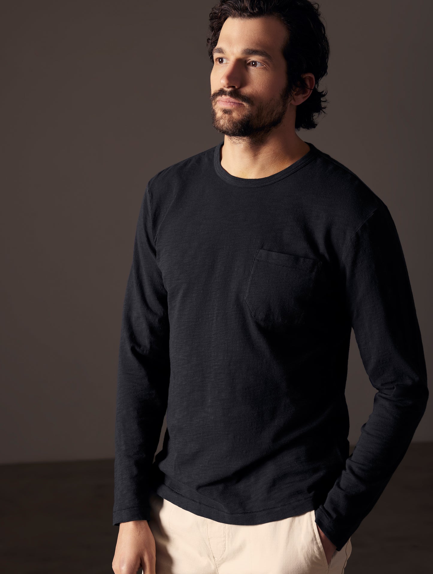 Front angled body view of man with hand in pant pocket wearing Slub Long-Sleeve Tee in Onyx Black from AETHER Apparel.