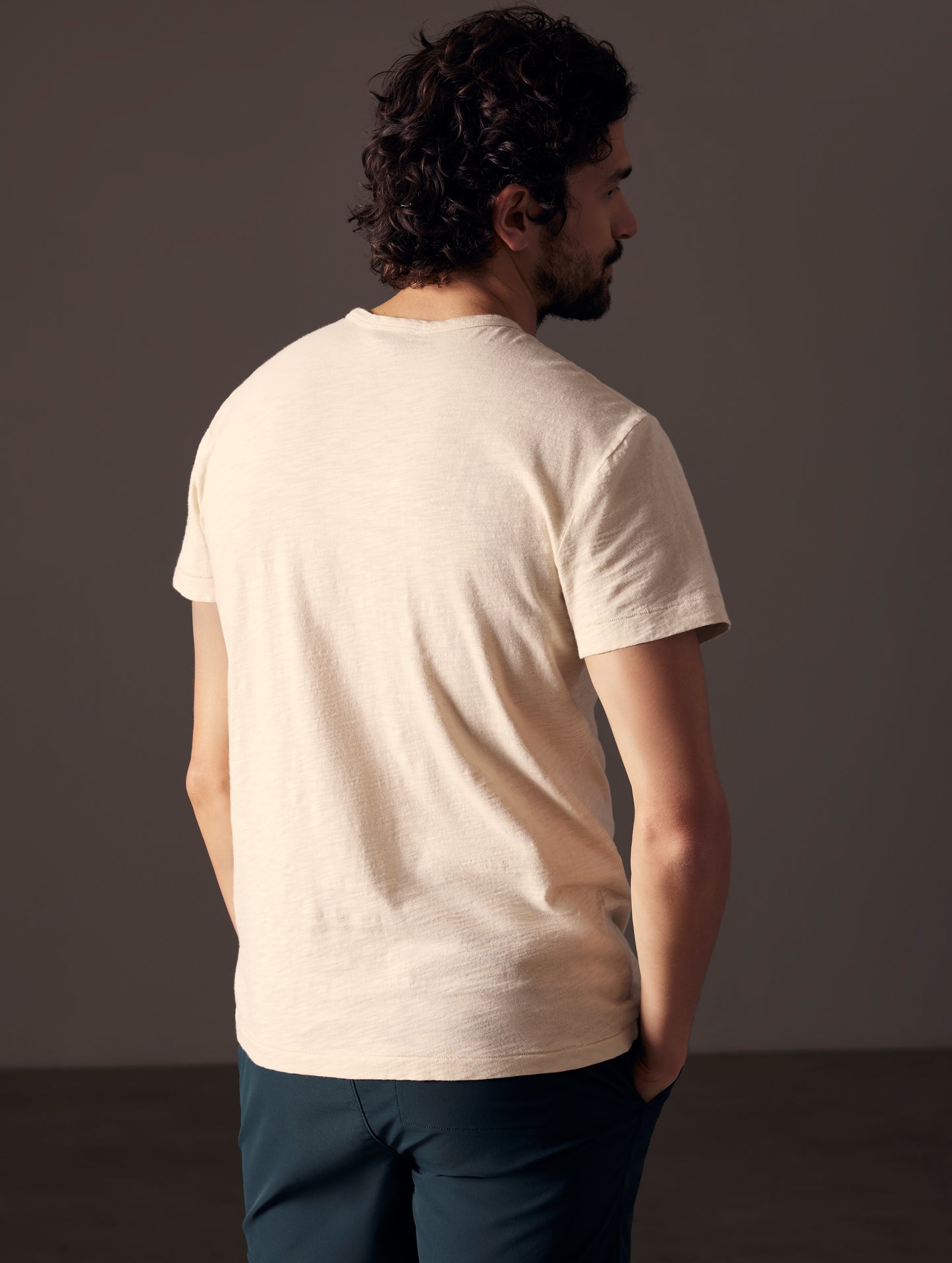 Rear angled body view of man wearing Slub Pocket Tee in Bone white from AETHER Apparel.