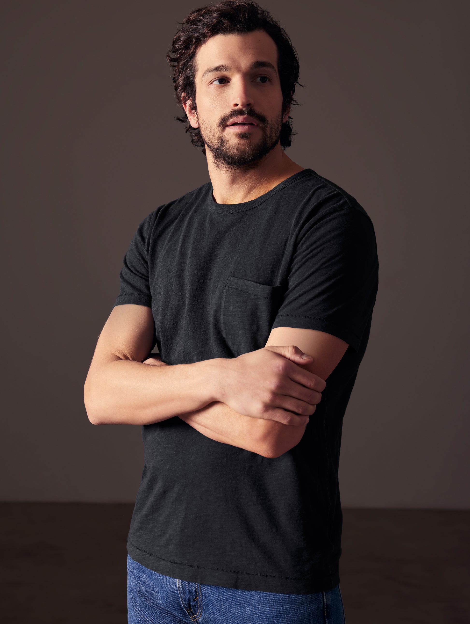 Front angled body view of man with arms crossed wearing Slub Pocket Tee in Onyx Black from AETHER Apparel.