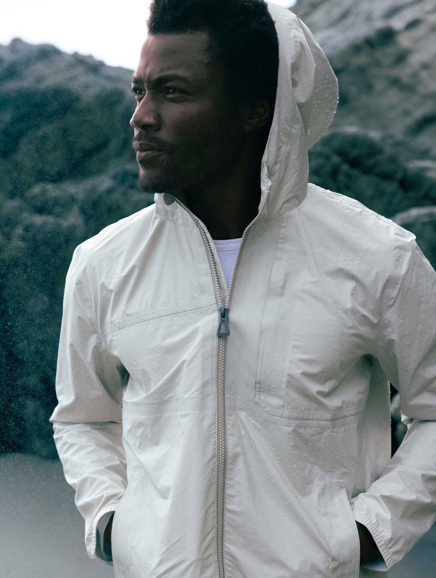 Front body outdoor lifestyle view of man wearing Storm All-Weather Jacket in Bone white from AETHER Apparel.